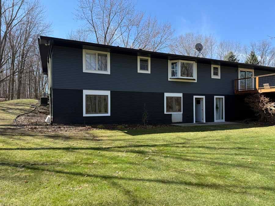 Dark two-story house with black siding and white-trimmed windows on a grassy lot under a clear sky