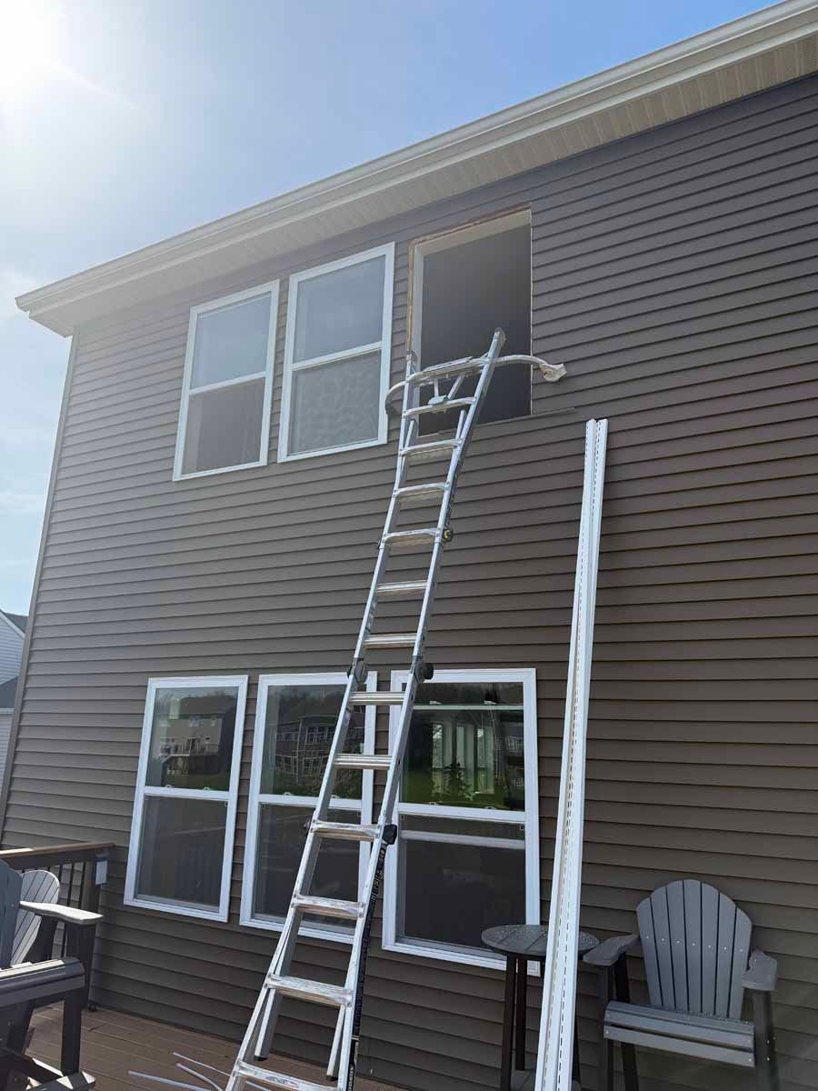 Ladder leaning to second-story window on a tan house, with a person inside reaching out.