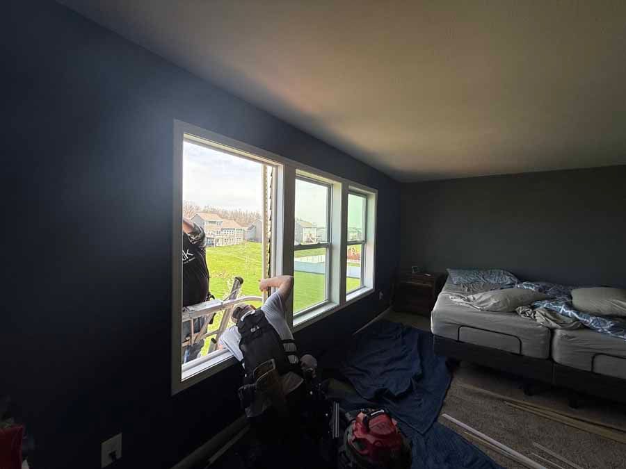Dim bedroom with open window, desk chair, and unmade bed by the wall.