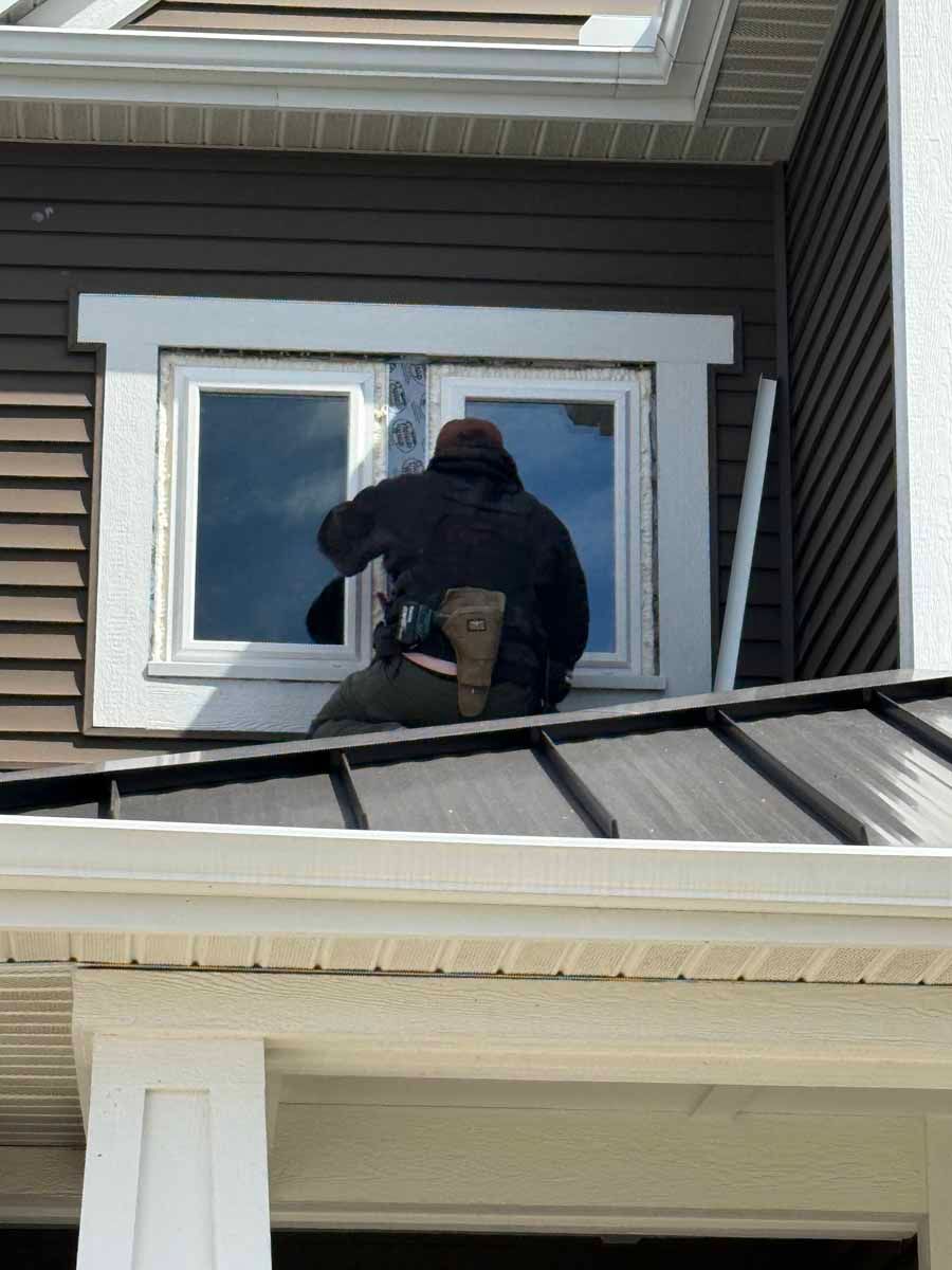 Person working on a second-story window from the roof of a house.
