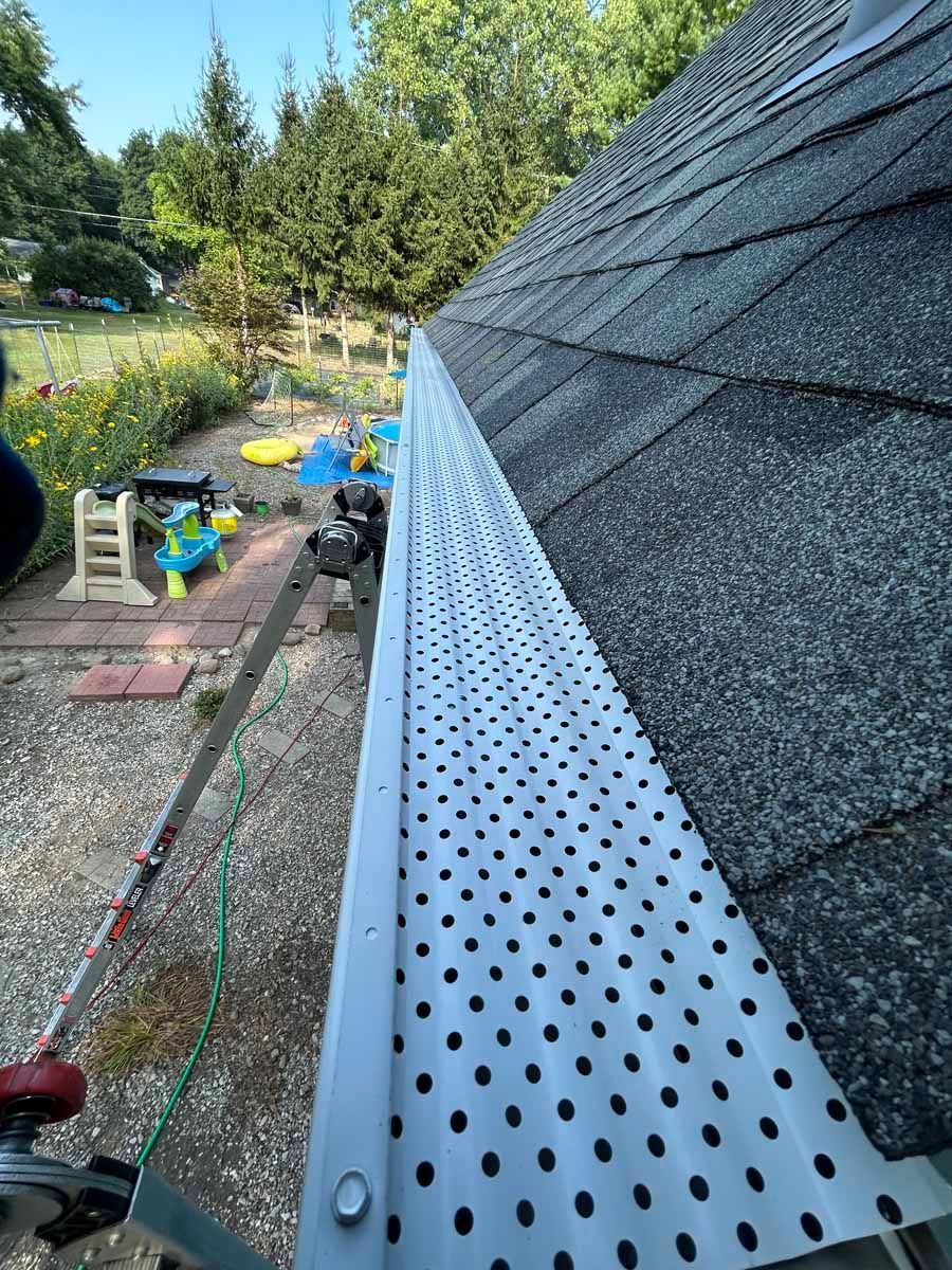 Gutter and roof edge on a house, with a ladder, tools, and garden in the background