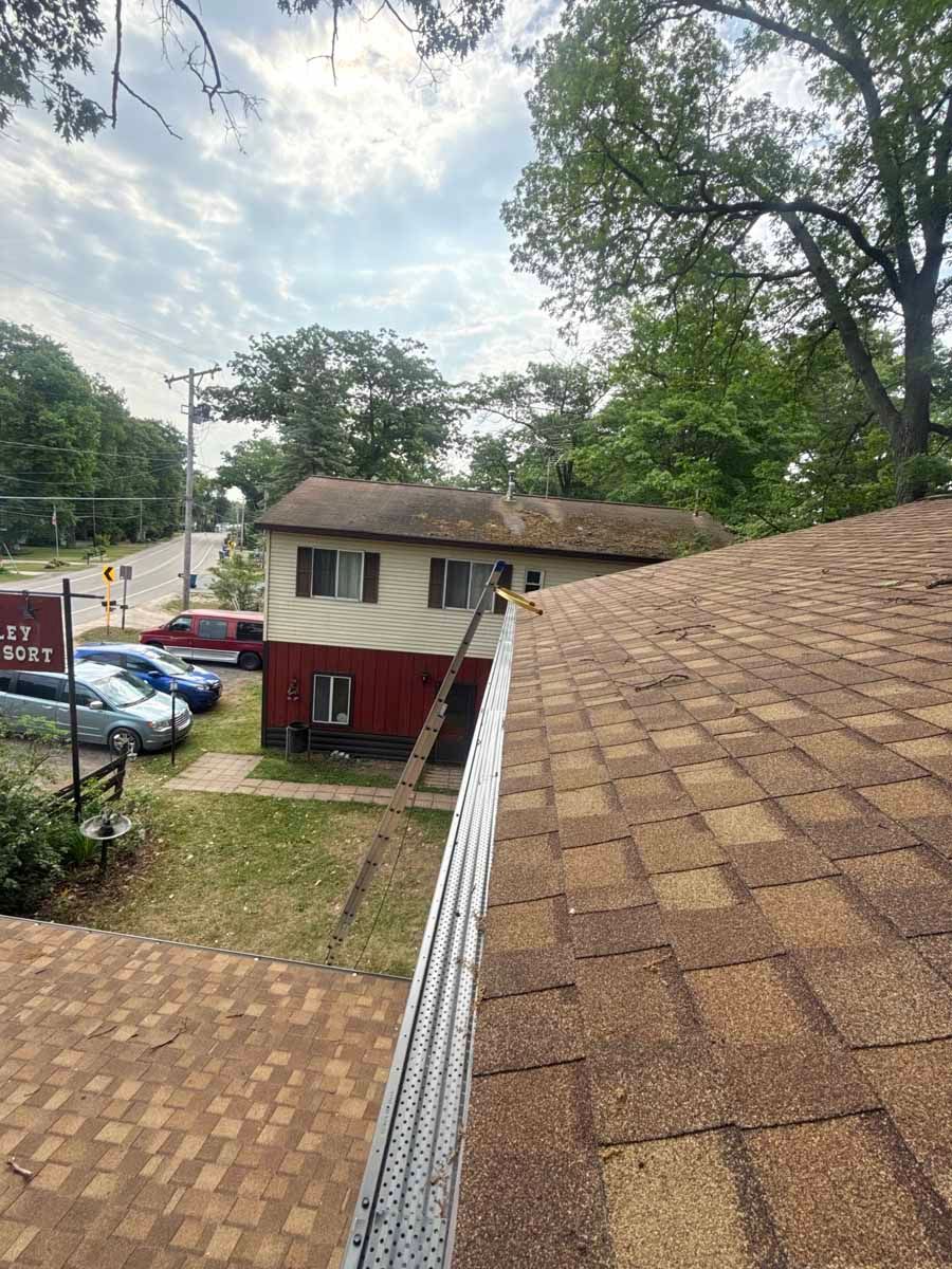Rooftop view of a suburban apartment building, parked cars, and tall trees under a cloudy sky