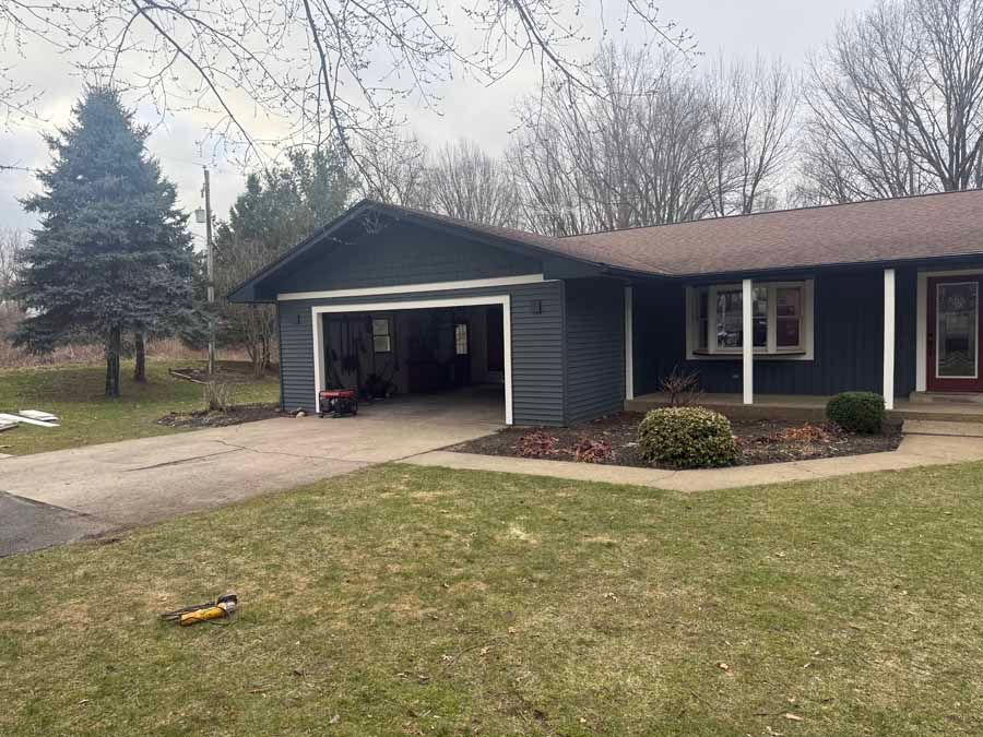 Single-story dark blue house with an open garage, front lawn, and overcast sky