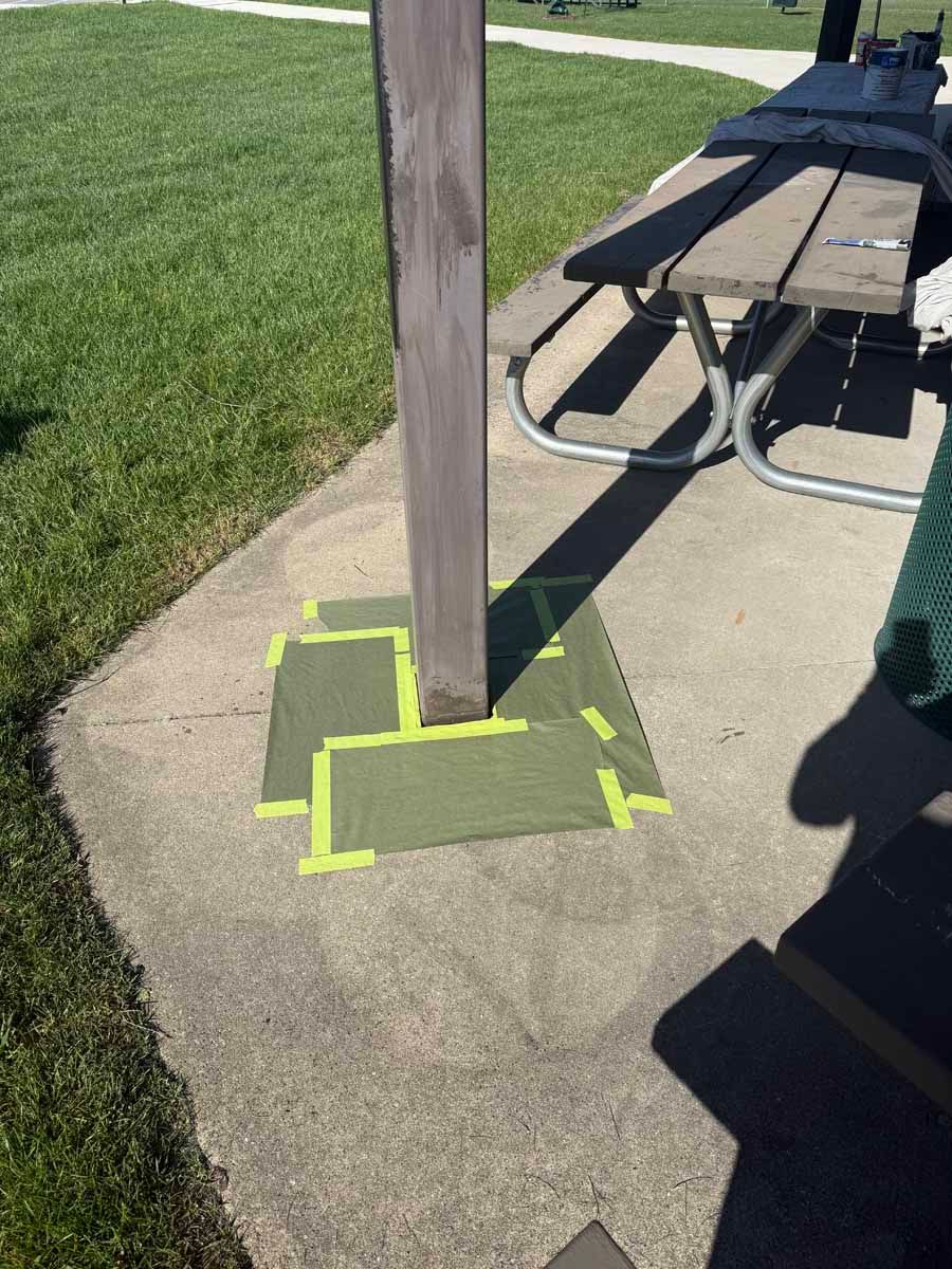 Wooden post on a concrete pad beside a picnic table and grass, marked with bright yellow tape.
