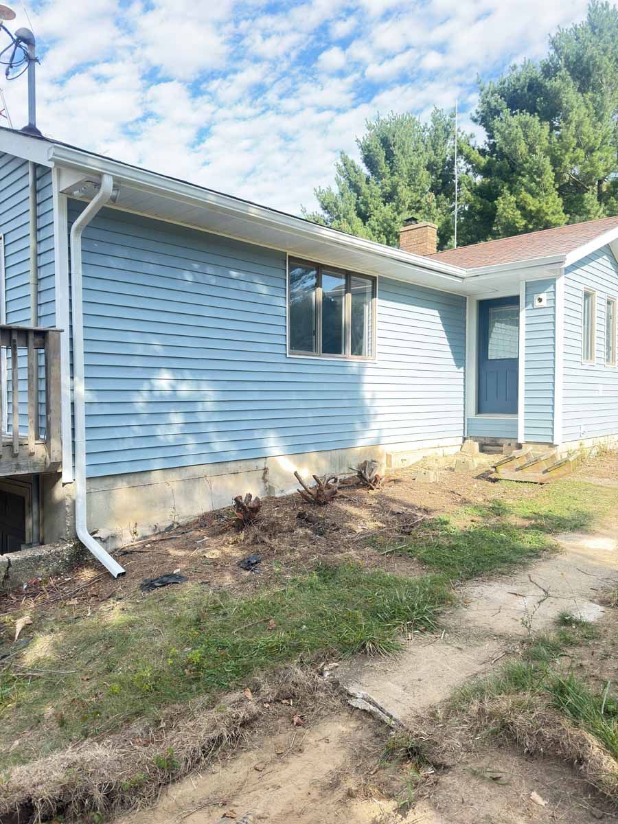Blue house exterior with damaged landscaping and a dirt path by the side wall