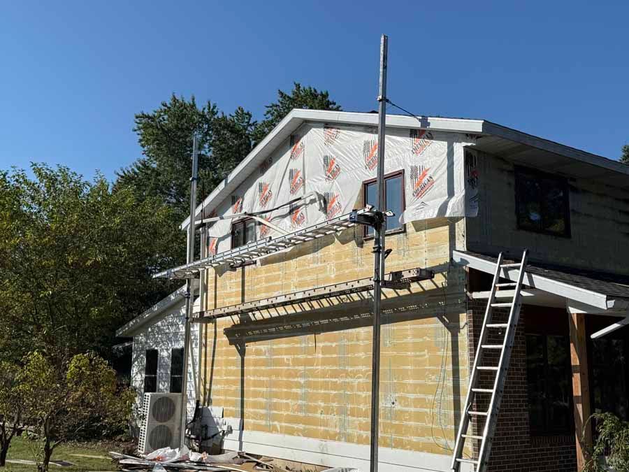 House exterior under renovation with scaffolding, ladder, and exposed wall insulation.