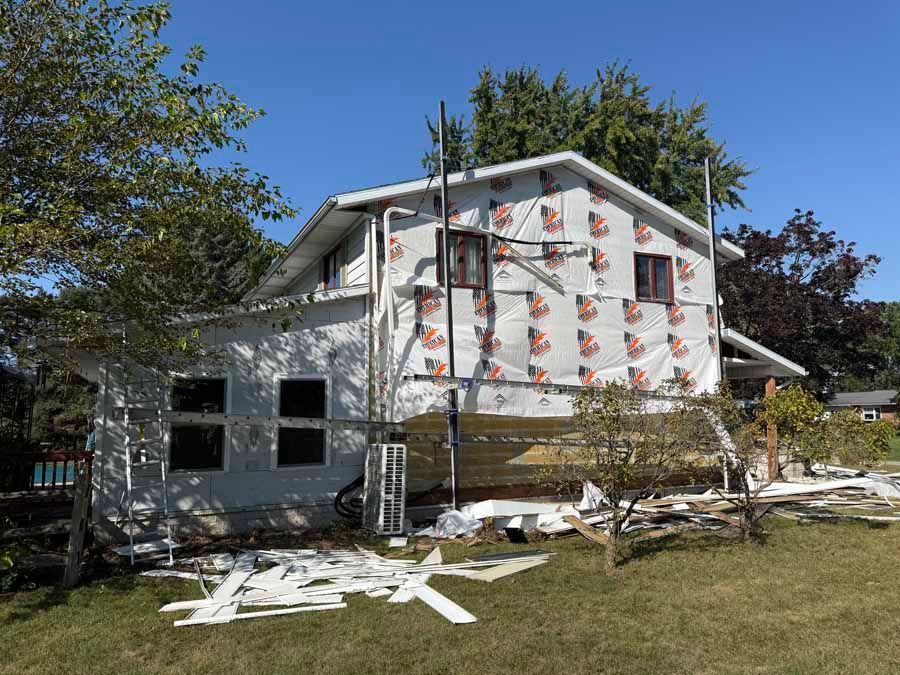 Two-story house under renovation with white siding, scaffolding, and construction debris on the lawn.