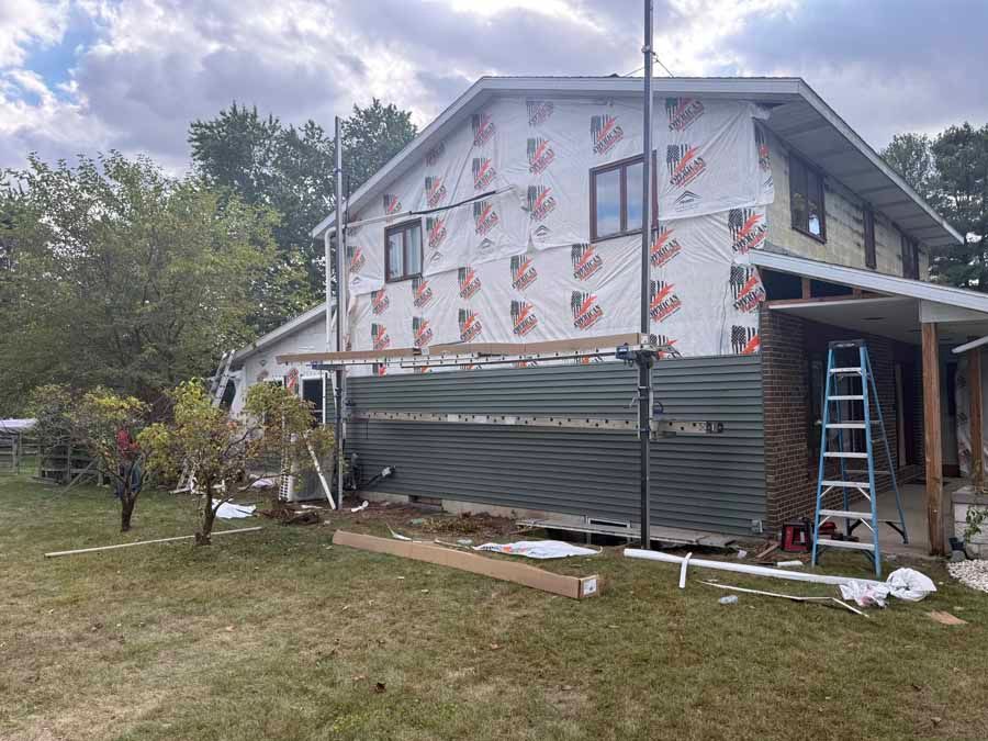 House under construction with white wrap, corrugated fencing, and a ladder on the right side of the yard