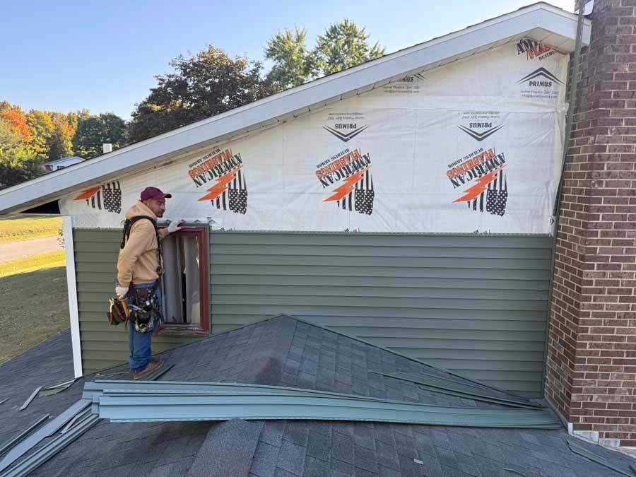 Worker installing siding on a house exterior beside a brick chimney