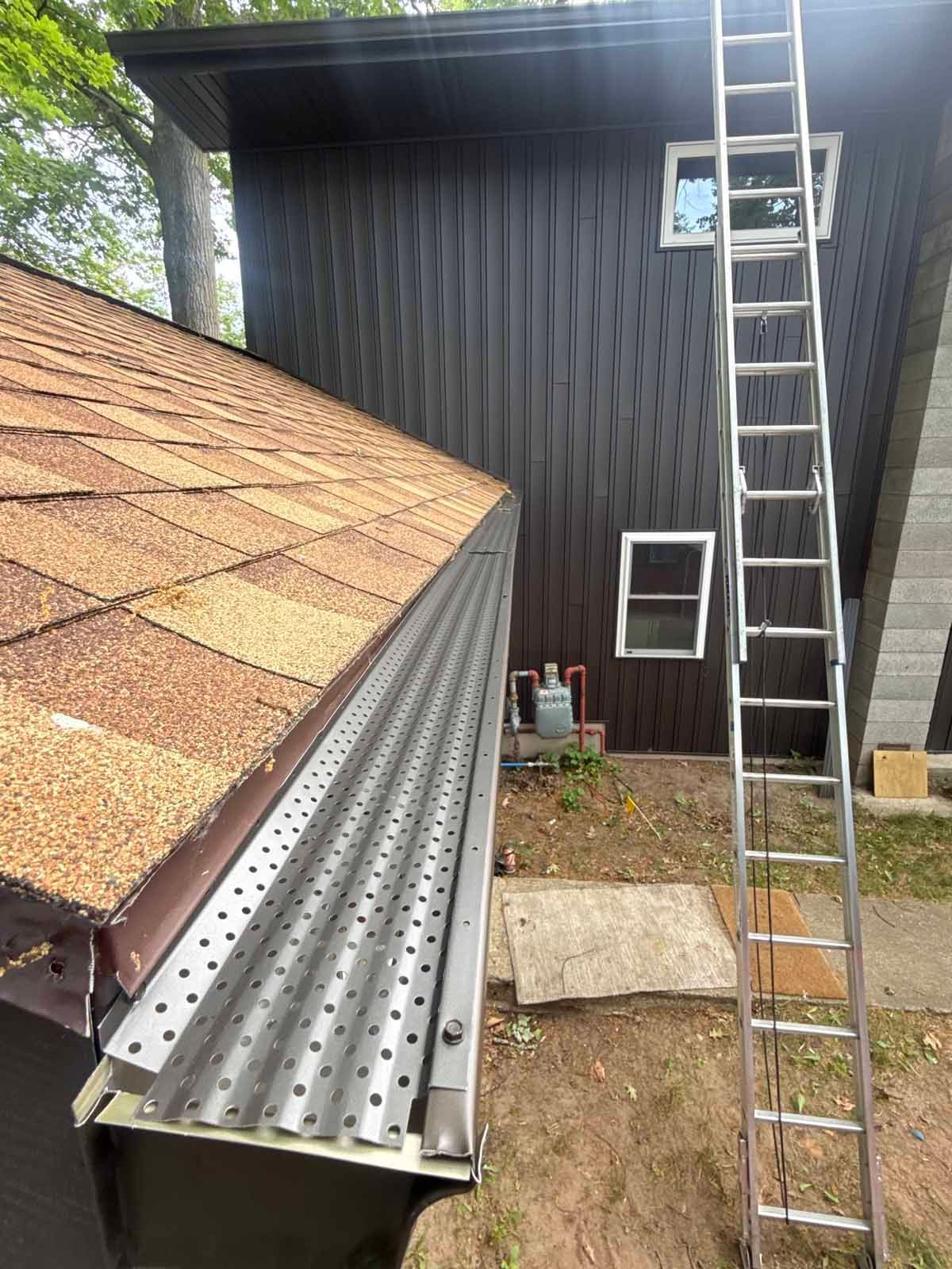 Roof repair with ladders beside a dark-sided house and a small window