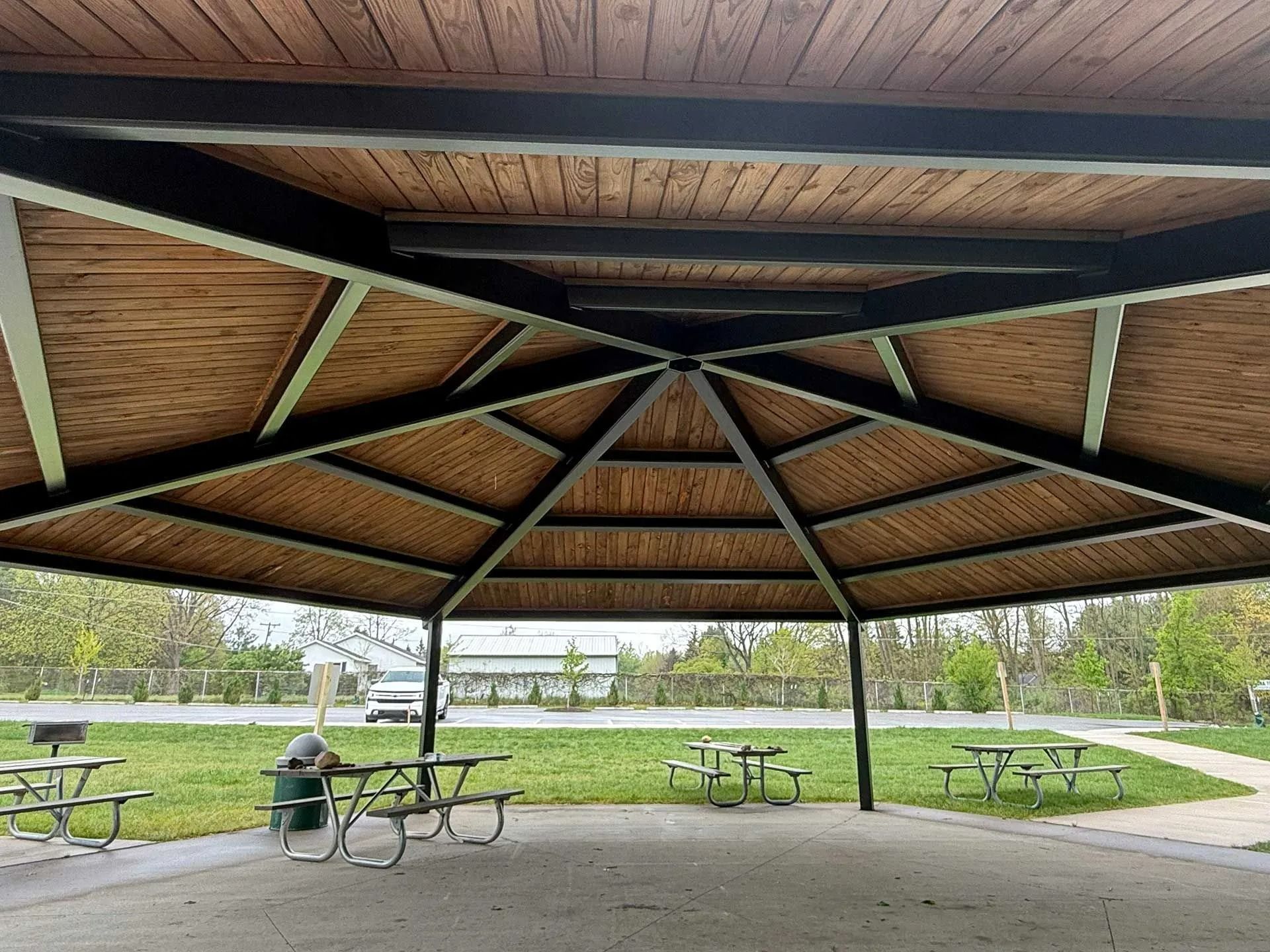 Covered picnic shelter with tables and benches overlooking a grassy park and path