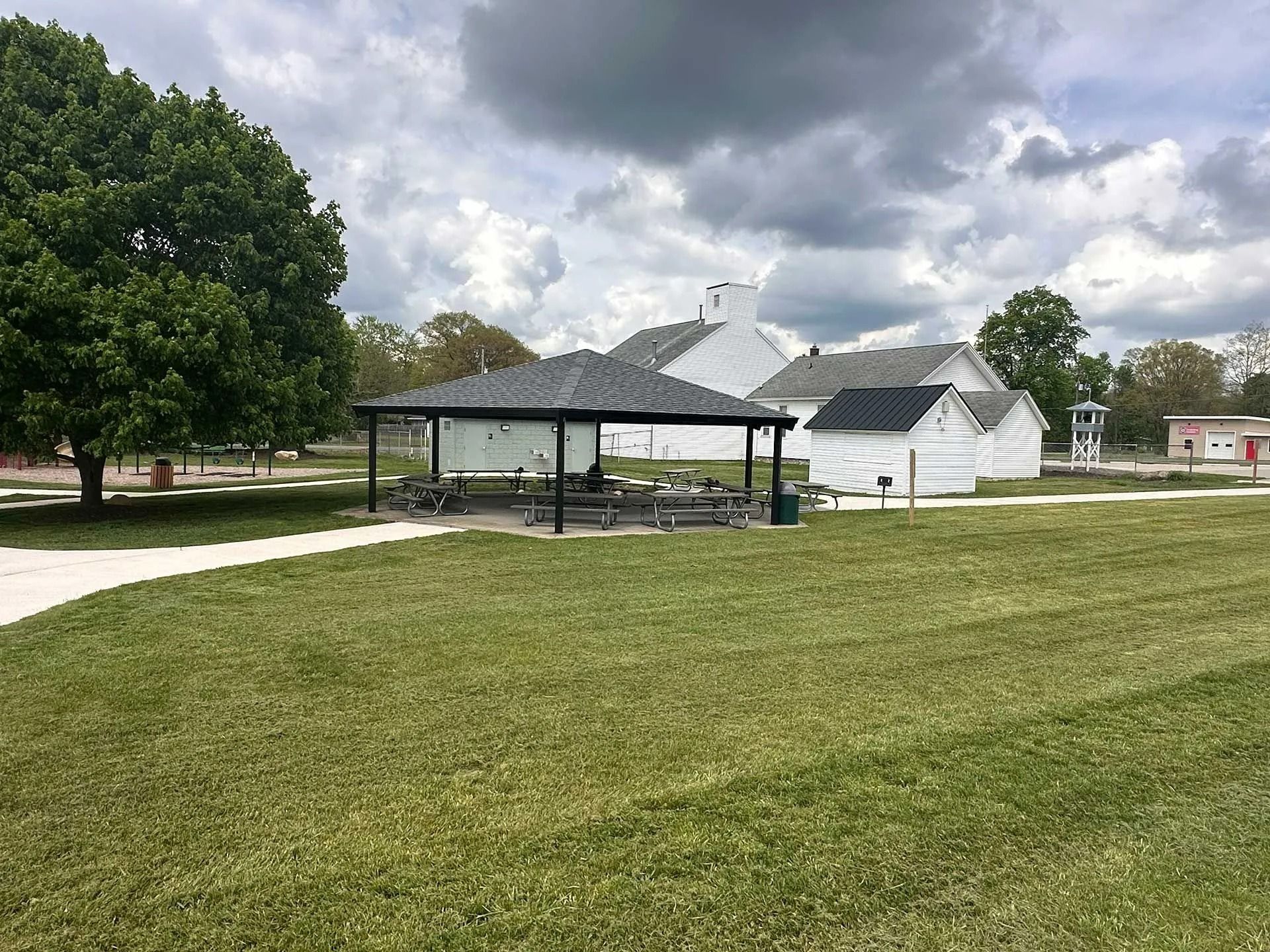 Park pavilion beside a white building on a grassy field under cloudy skies