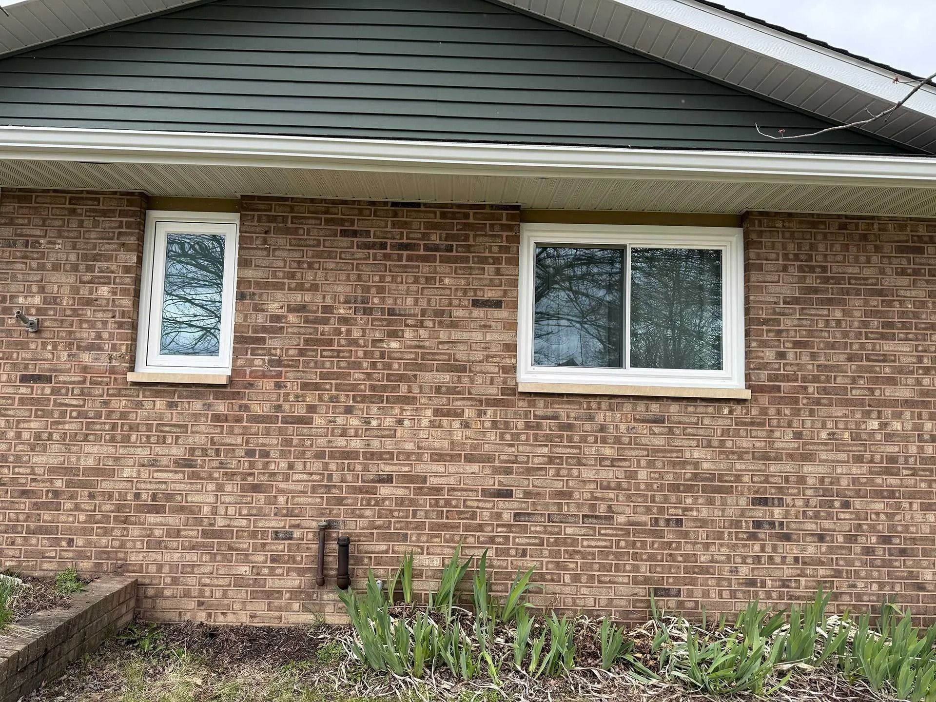 Brick house exterior with two windows and a small garden bed beneath the wall