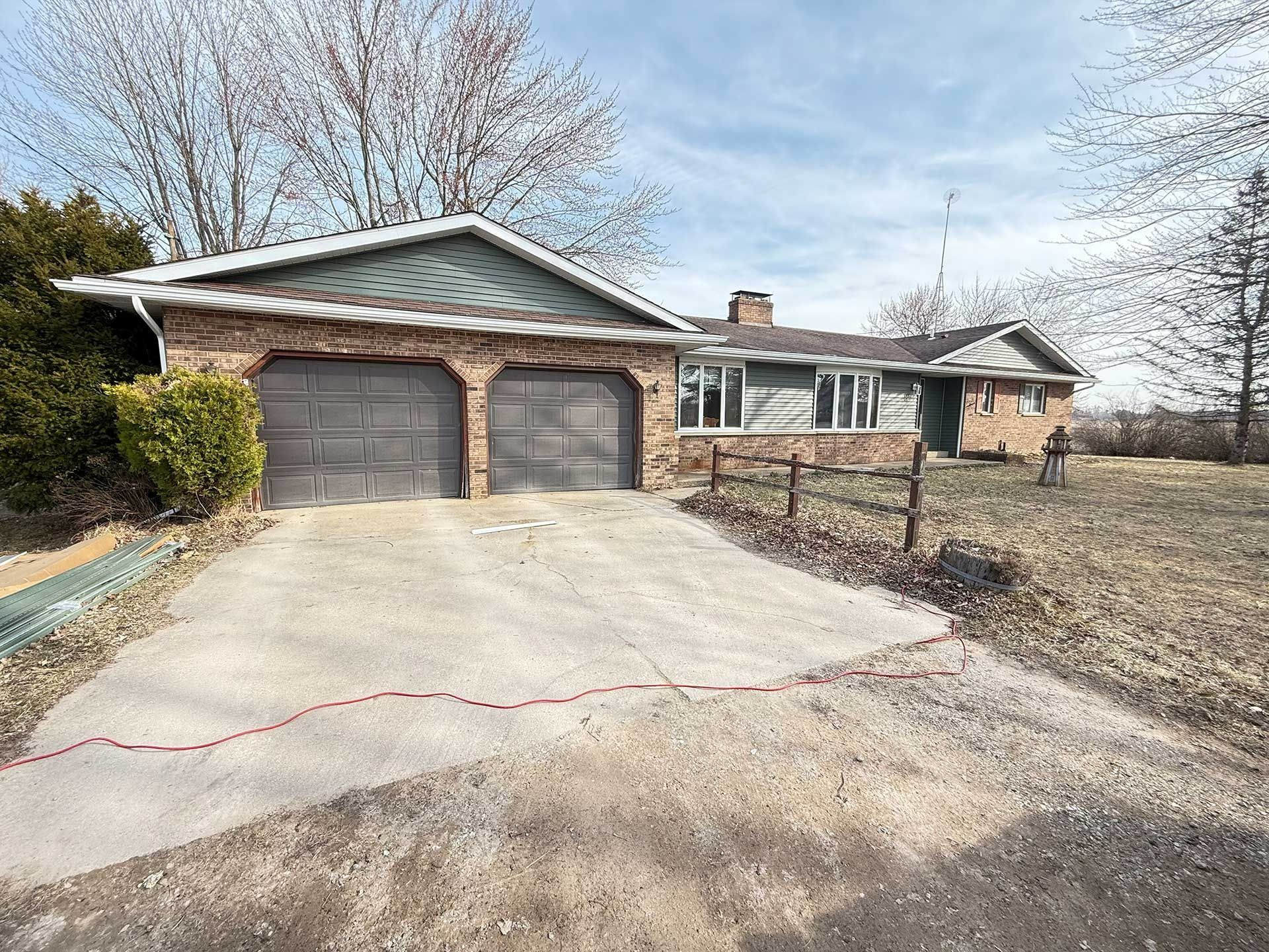 Suburban house with a two-car garage and long concrete driveway under a partly cloudy sky