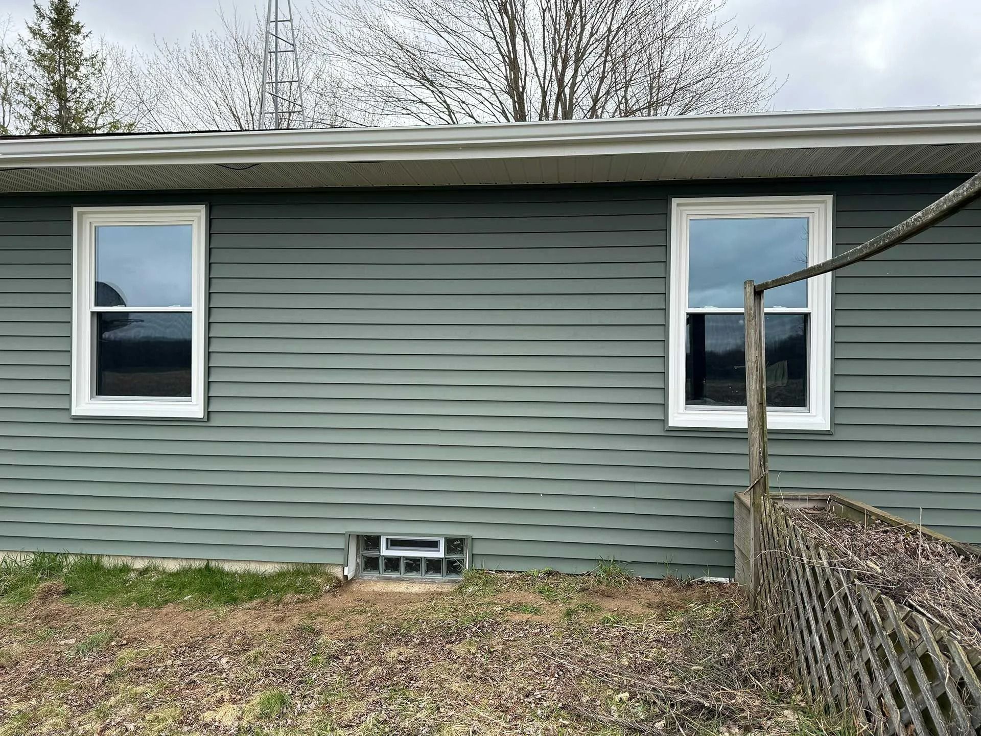 Gray house exterior with two windows, vinyl siding, and a chain-link fence in the foreground.