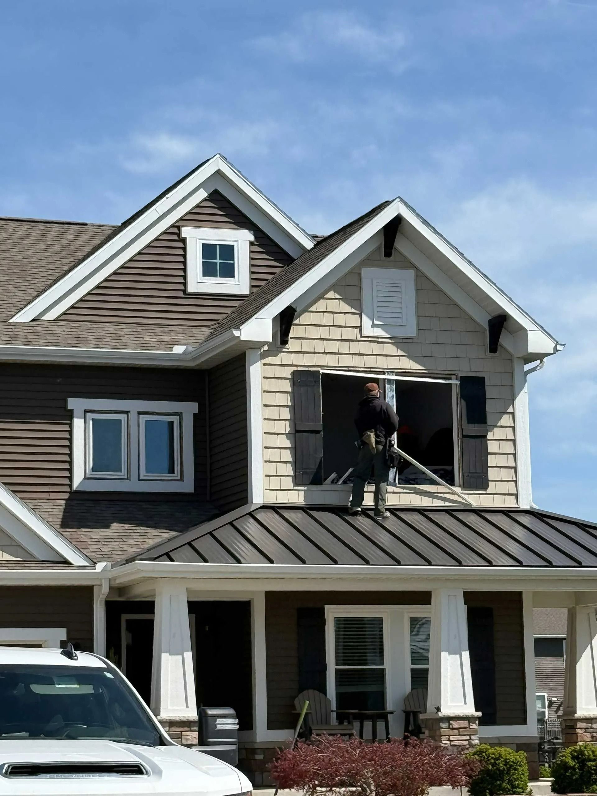Damaged upper-story window on a suburban house with a person standing in the opening