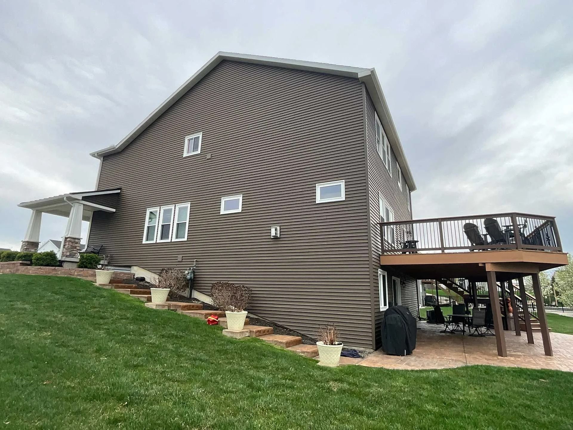 Brown wavy-sided house with deck on a grassy hill under a cloudy sky