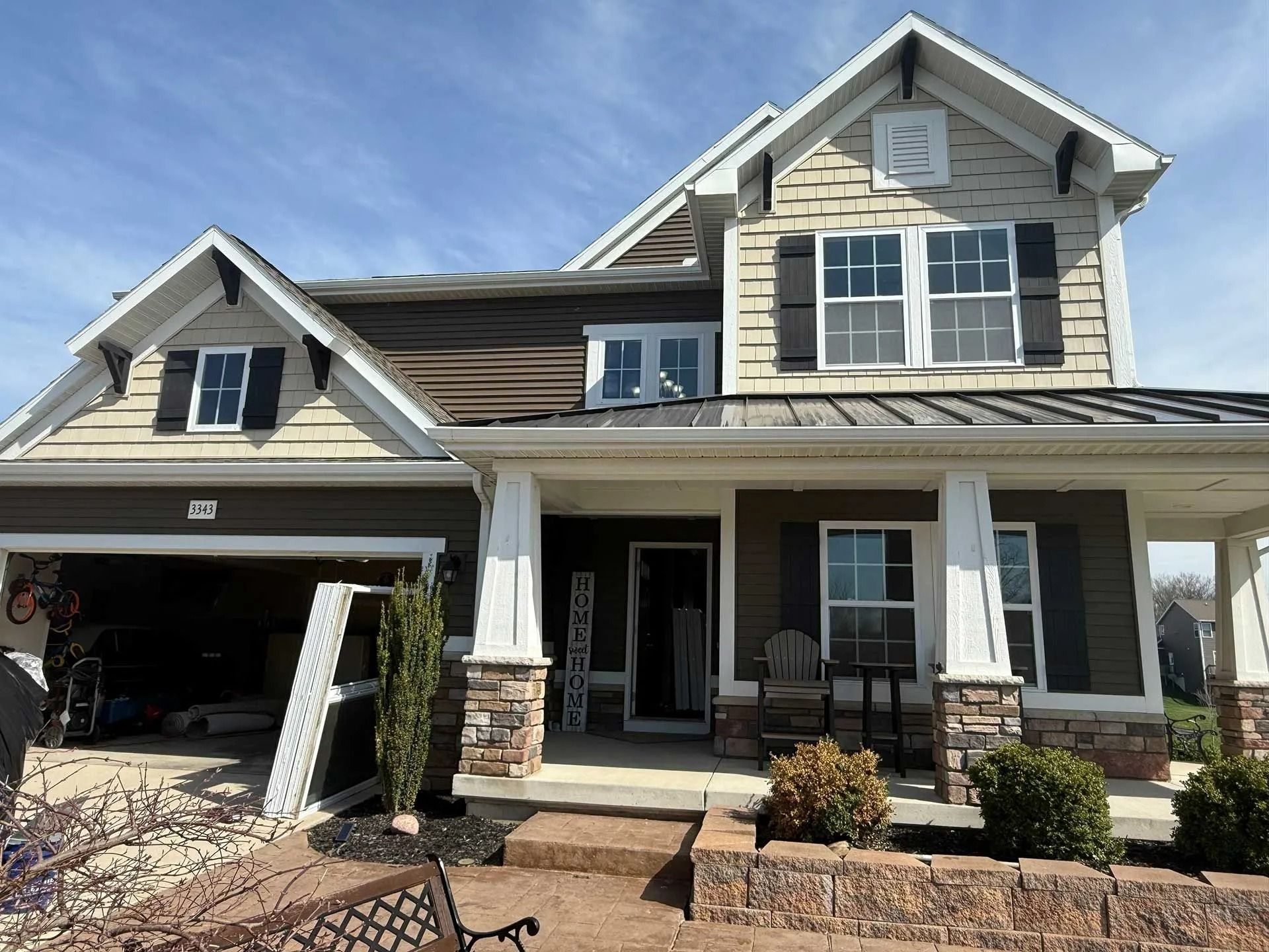 Suburban two-story house with gray siding, a front porch, and an attached garage under a clear blue sky