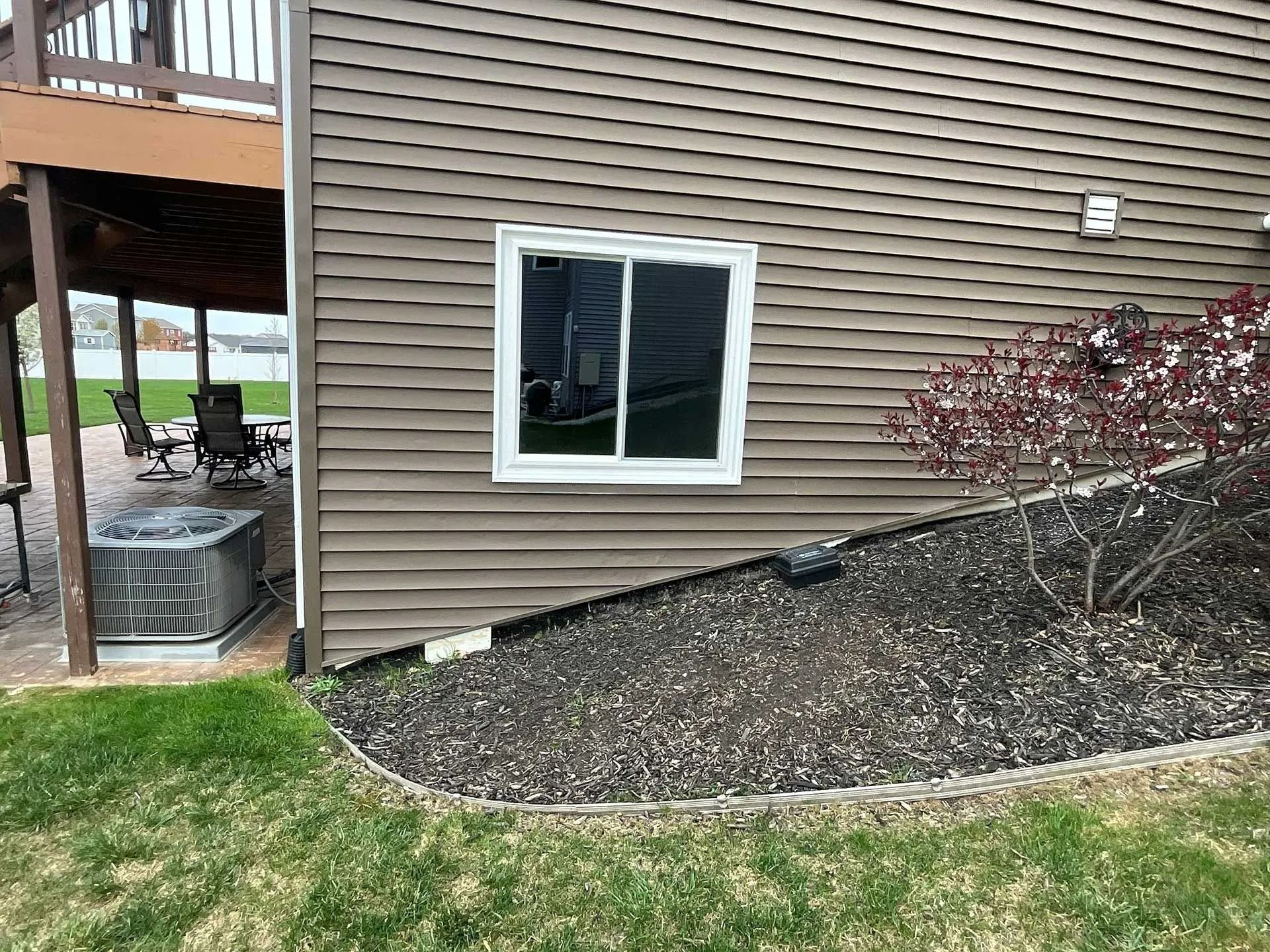 House exterior with brown siding, window, covered patio, and gravel landscaping beside grass