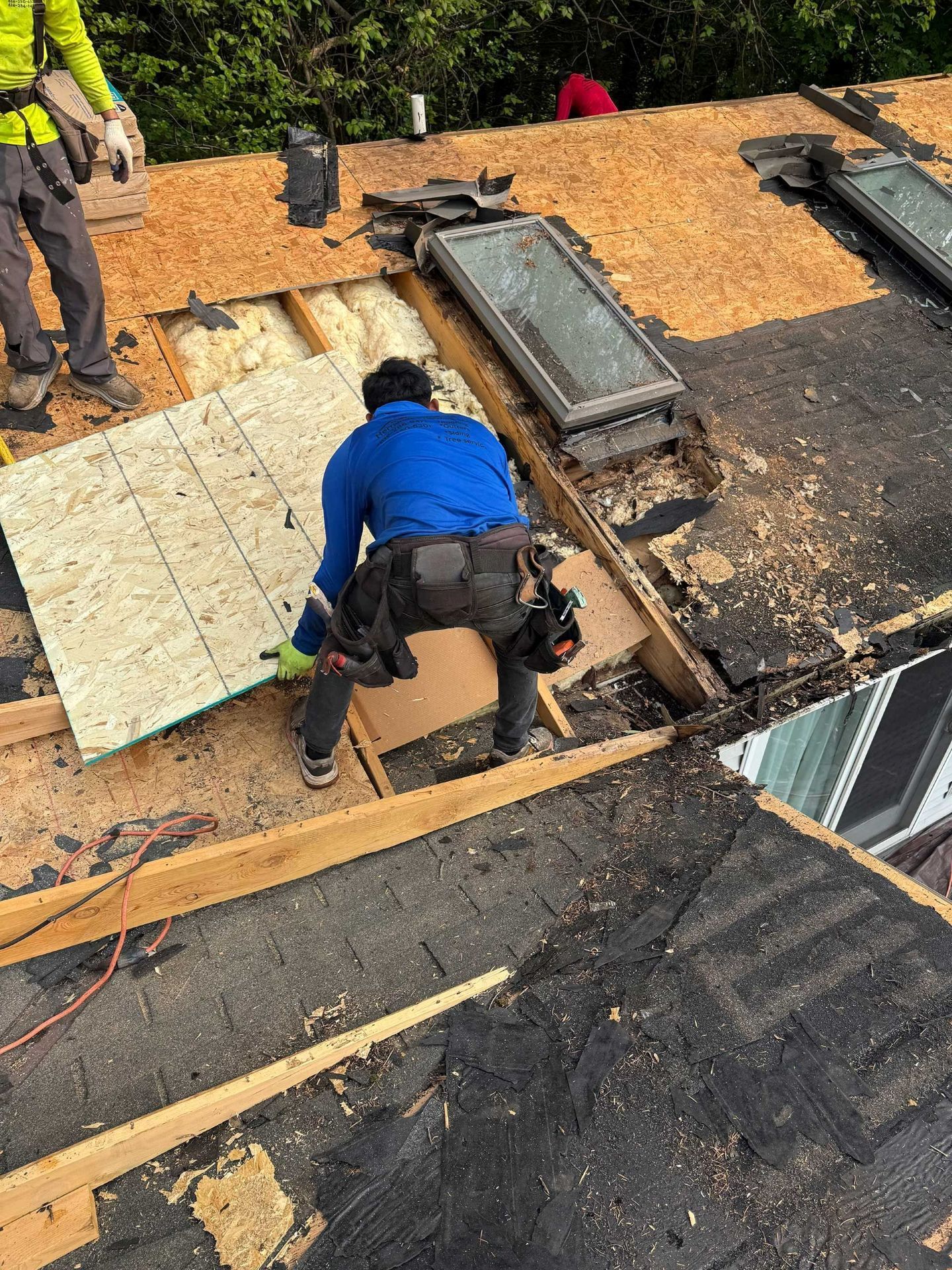 Two roofers install roofing panels on a partially stripped roof deck.