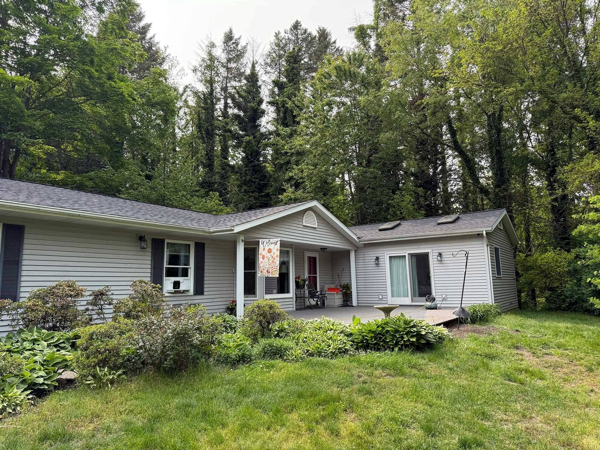 Single-story house with gray siding and white trim, surrounded by green lawn and tall trees.