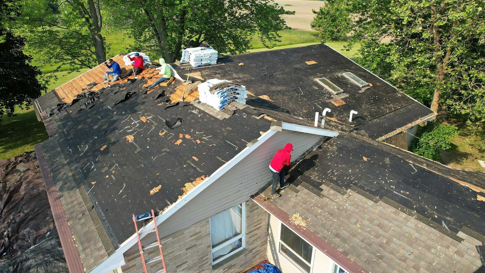 Workers repairing a damaged roof with tarps and materials on a house surrounded by trees