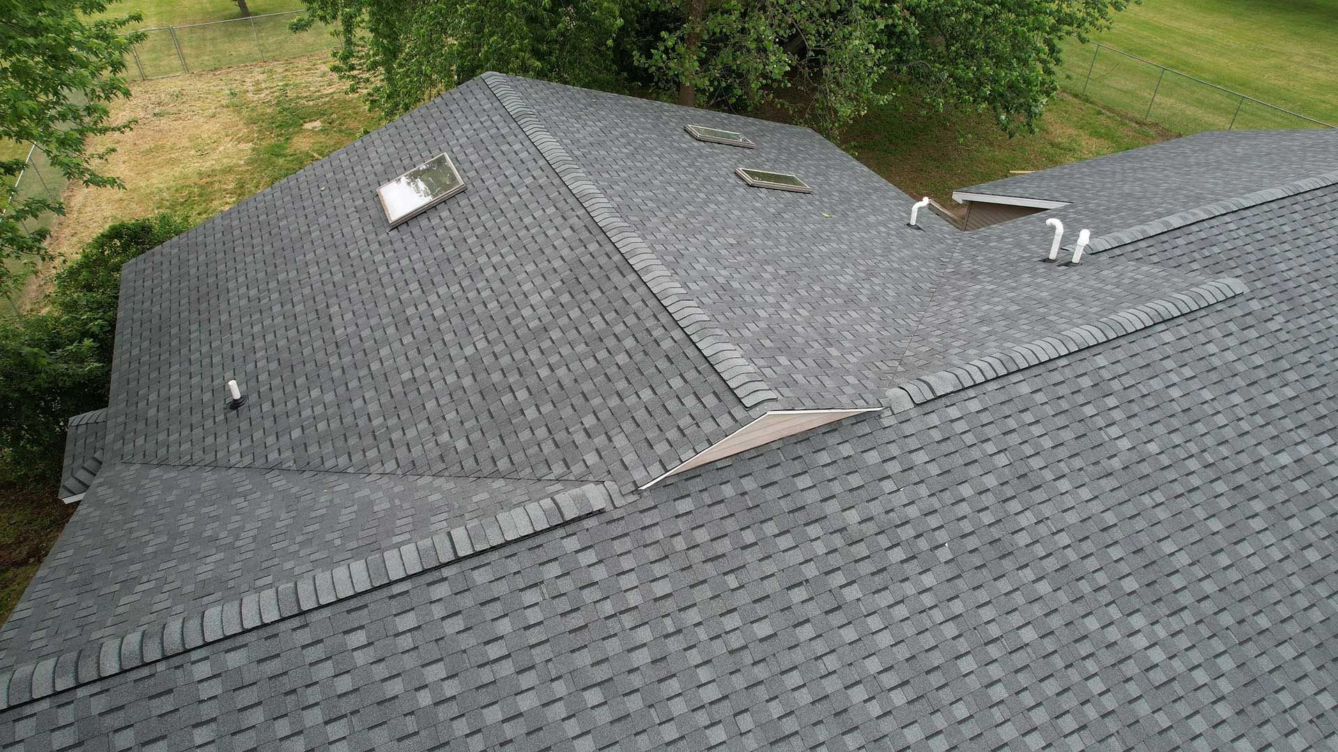 Gray shingled house roof with skylights and trees in the background
