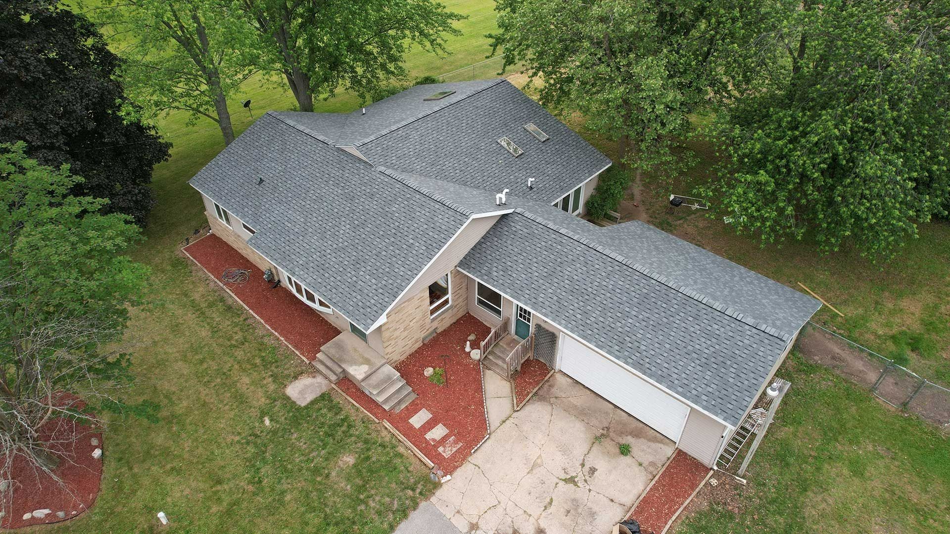 Aerial view of a gray-roofed brick house with a red front porch and surrounding trees