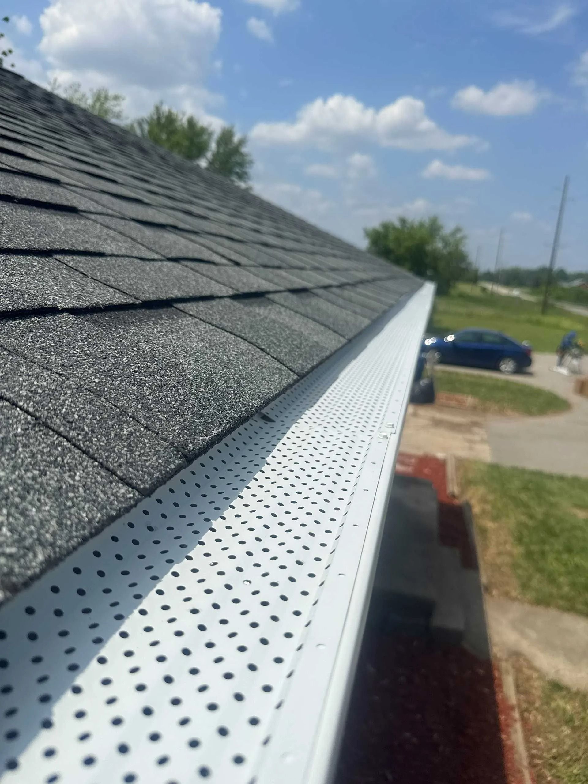 Close-up of a shingled roof with white perforated gutter along the edge under a blue sky