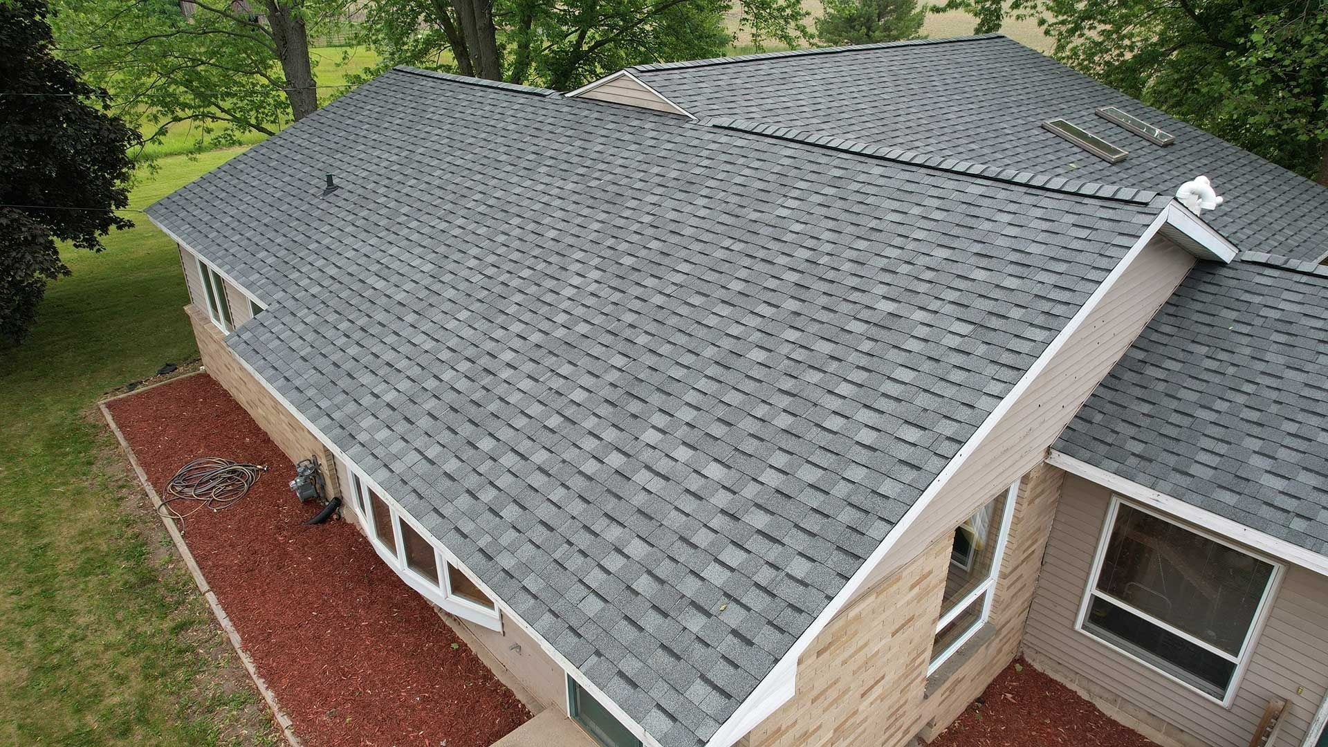 Aerial view of a house roof with gray shingles, skylights, and a red mulch border below.