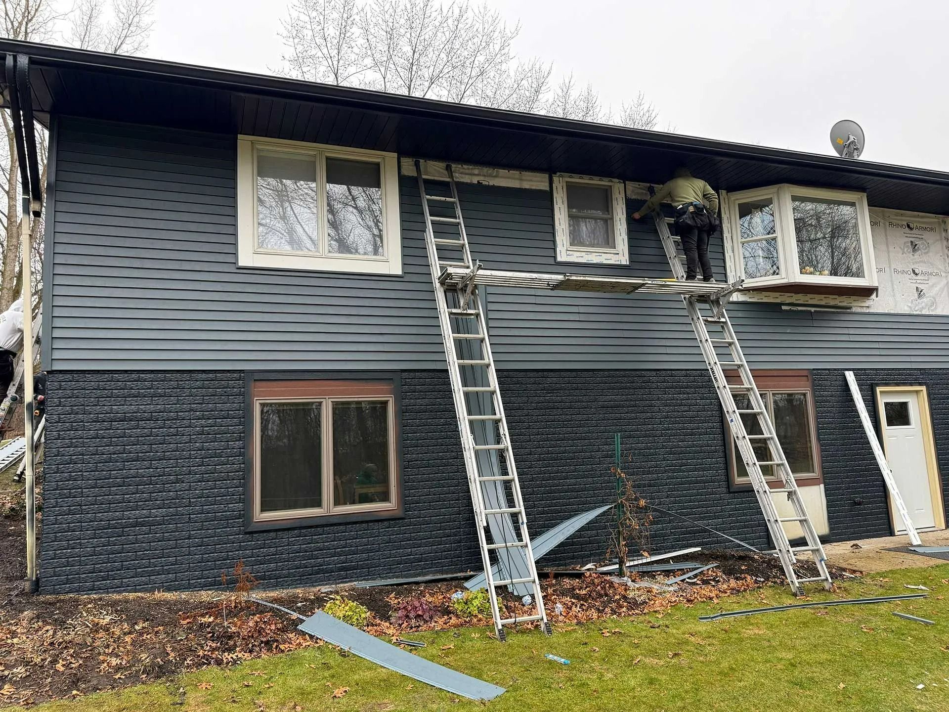 Two-story gray house with a ladder leaning to the second floor and a smaller ladder under the eaves