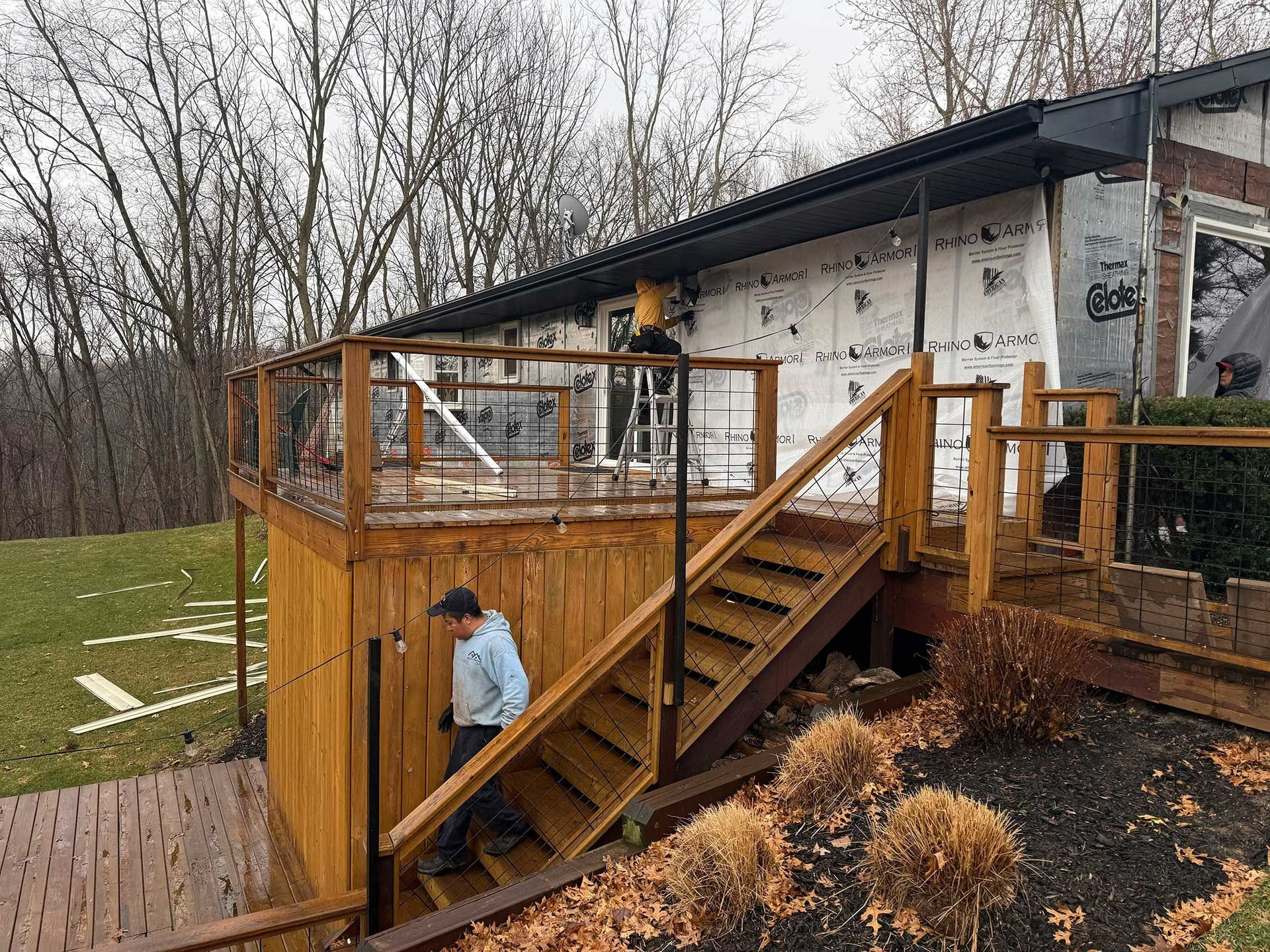 Person in blue jacket climbing wooden deck stairs beside a house in a wooded yard