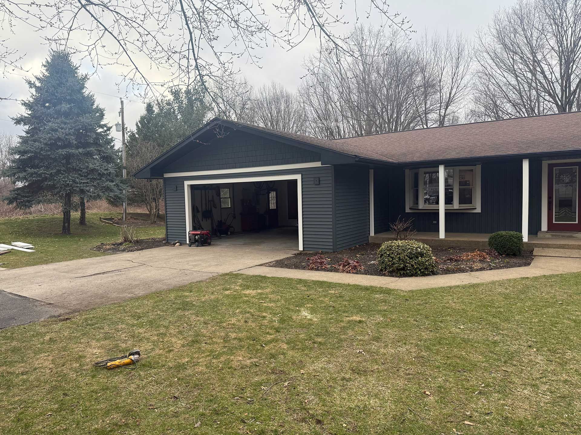 Single-story blue house with open garage, front porch, and winter yard under cloudy sky