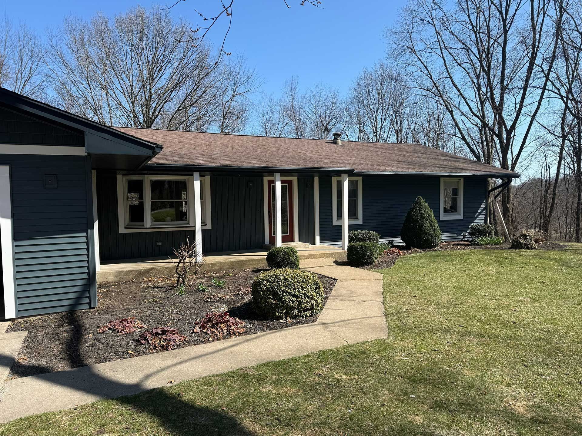 Single-story suburban house with blue siding, front walkway, and a grassy yard under a clear sky