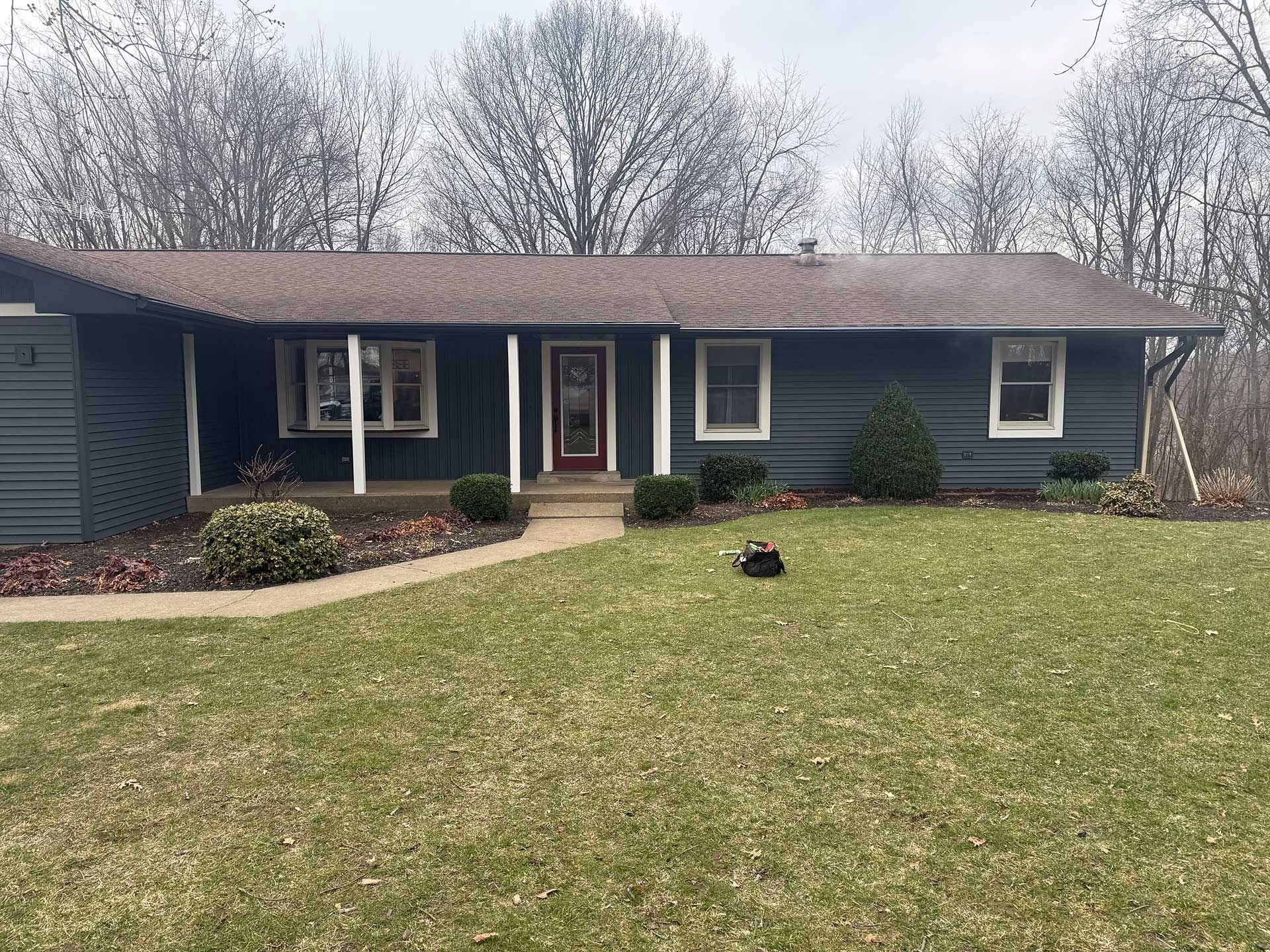 Single-story dark blue house with a front lawn and bare trees in the background.