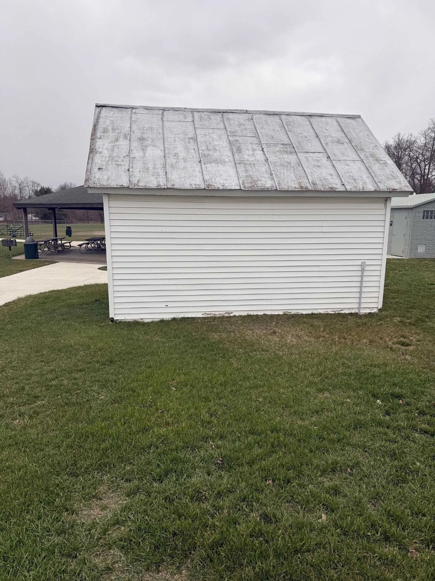 Small white wooden shed with a weathered metal roof in a grassy yard.