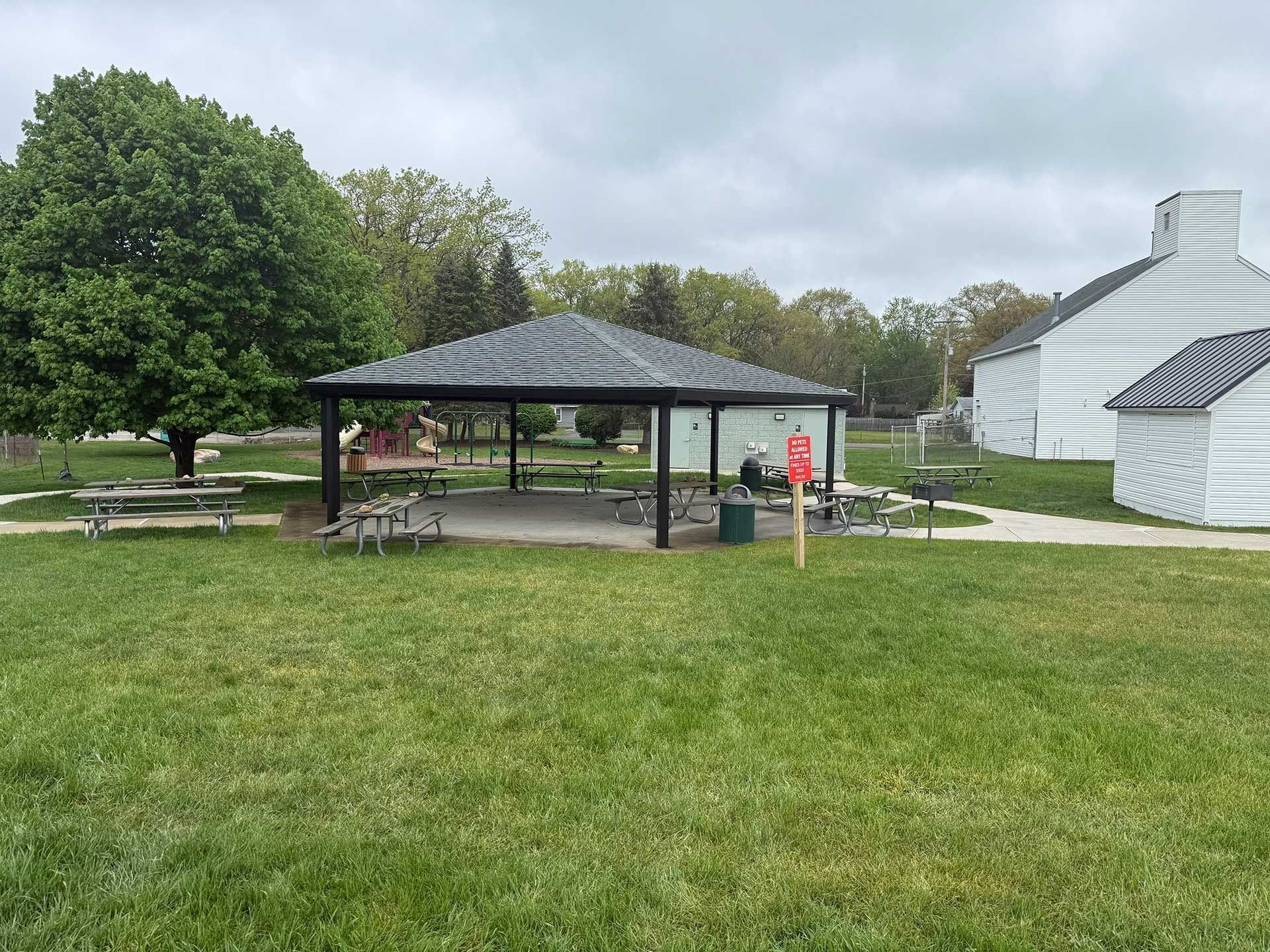 Park with a pavilion, picnic tables, and a large white structure beside a grassy field.