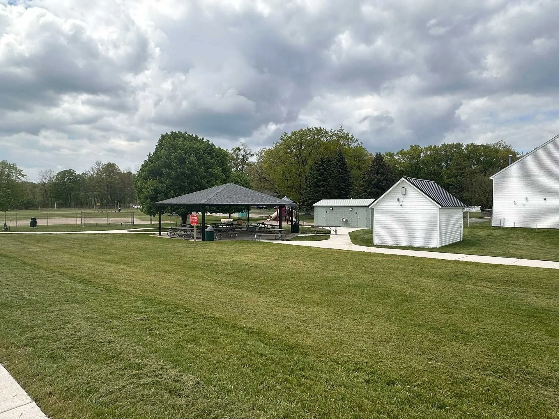 Grassy park with a picnic pavilion, small white sheds, and cloudy sky