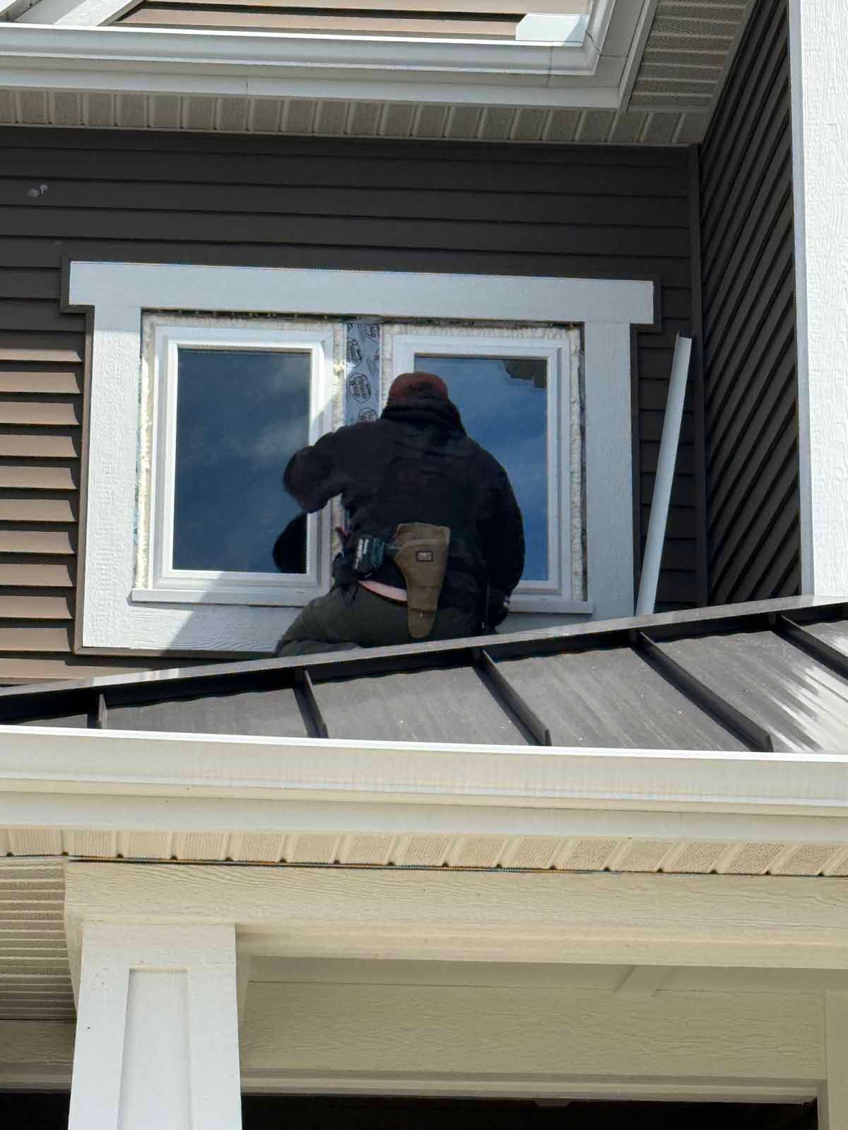 Person working on a second-story window on a house exterior, seen from below.