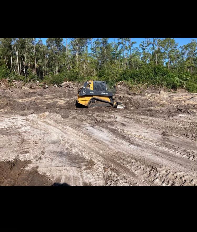 Yellow excavator stuck in muddy dirt clearing with trees in the background