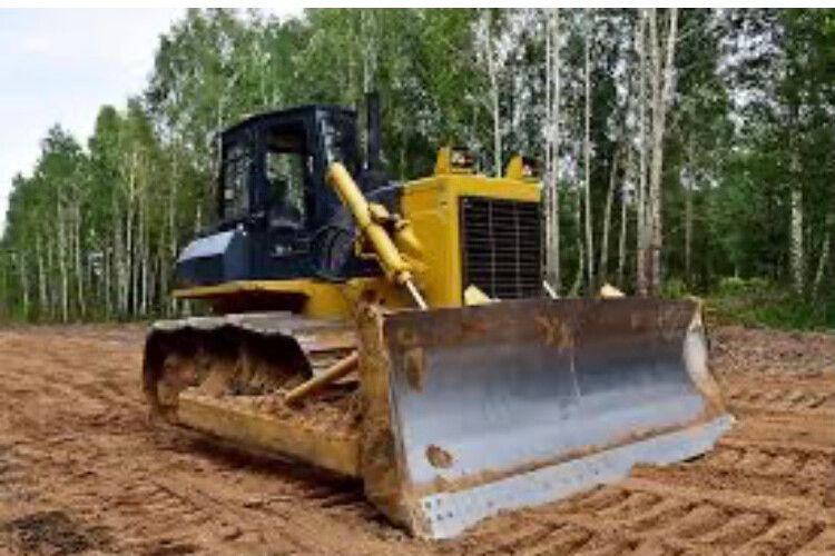 Yellow bulldozer on a dirt clearing with a raised blade, surrounded by trees.