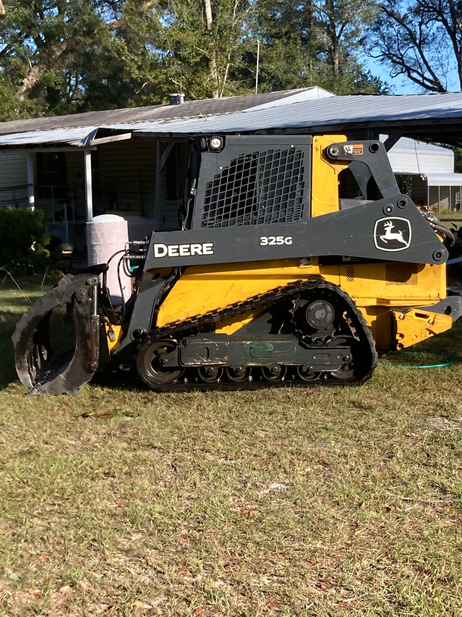 Yellow and black John Deere skid steer parked on grass beside a house