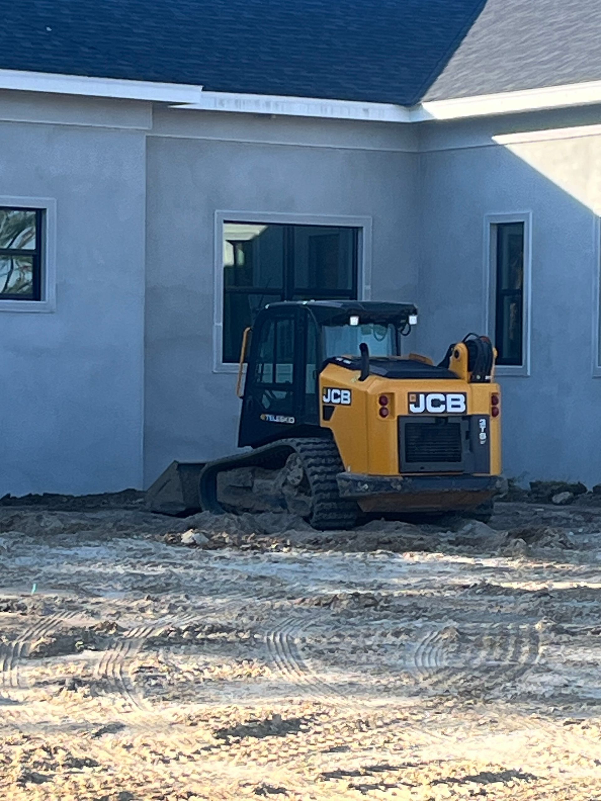 Yellow JCB skid steer loading dirt beside a house under construction