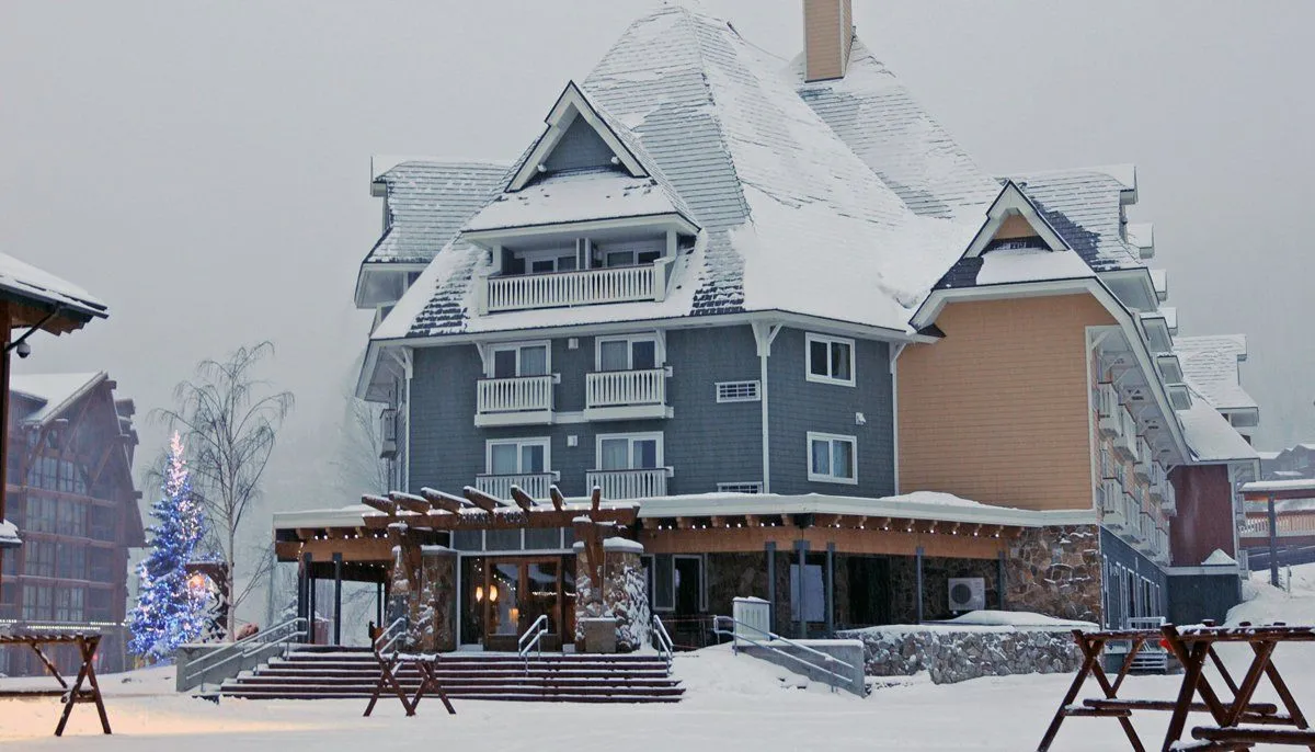 Snow-covered chalet-style lodge with gray and tan siding in a winter scene