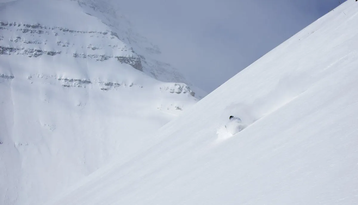 Snowy mountain slope with a lone skier carving through deep powder under a cloudy sky