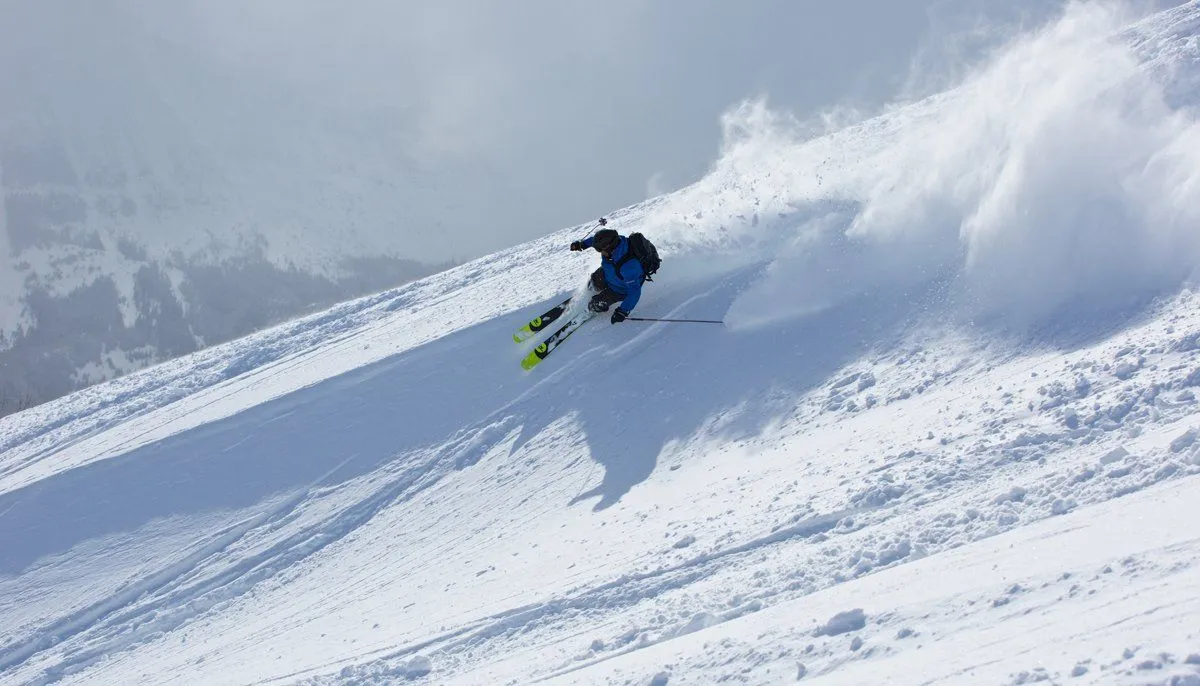 Skier carving a turn through fresh powder on a snowy mountain slope