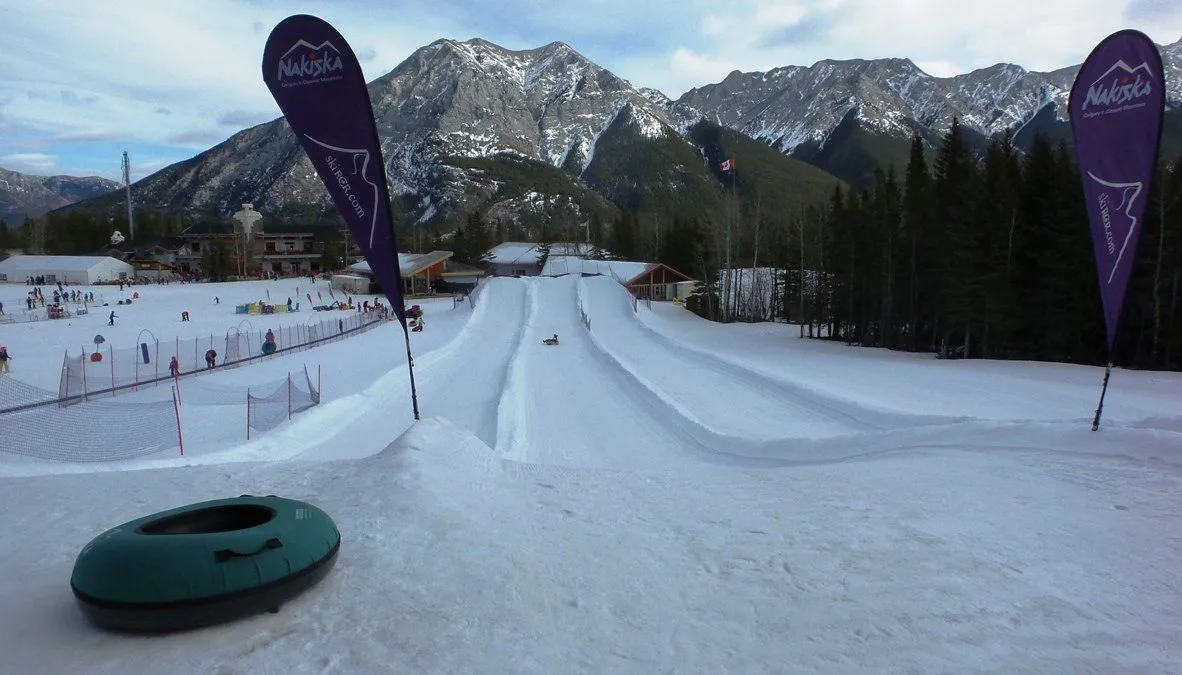 Snow tubing lanes at a mountain resort with purple flags and a forested backdrop