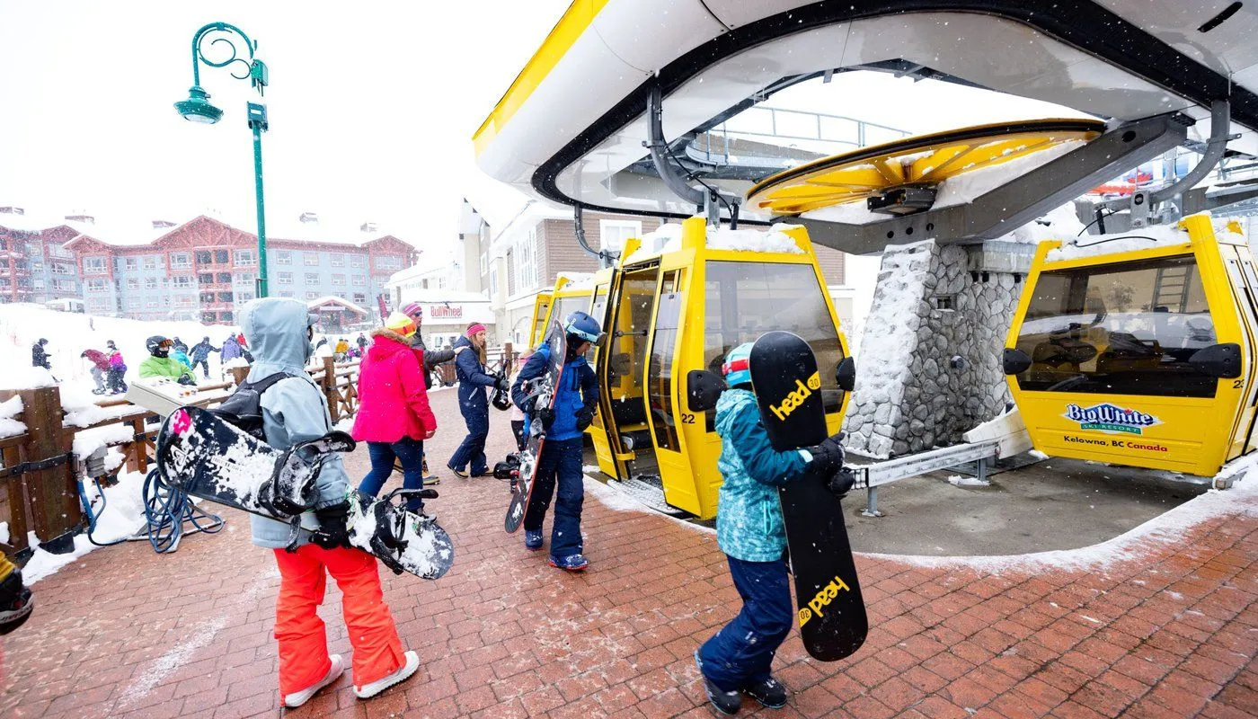 People boarding yellow gondola lifts in a snowy mountain resort station