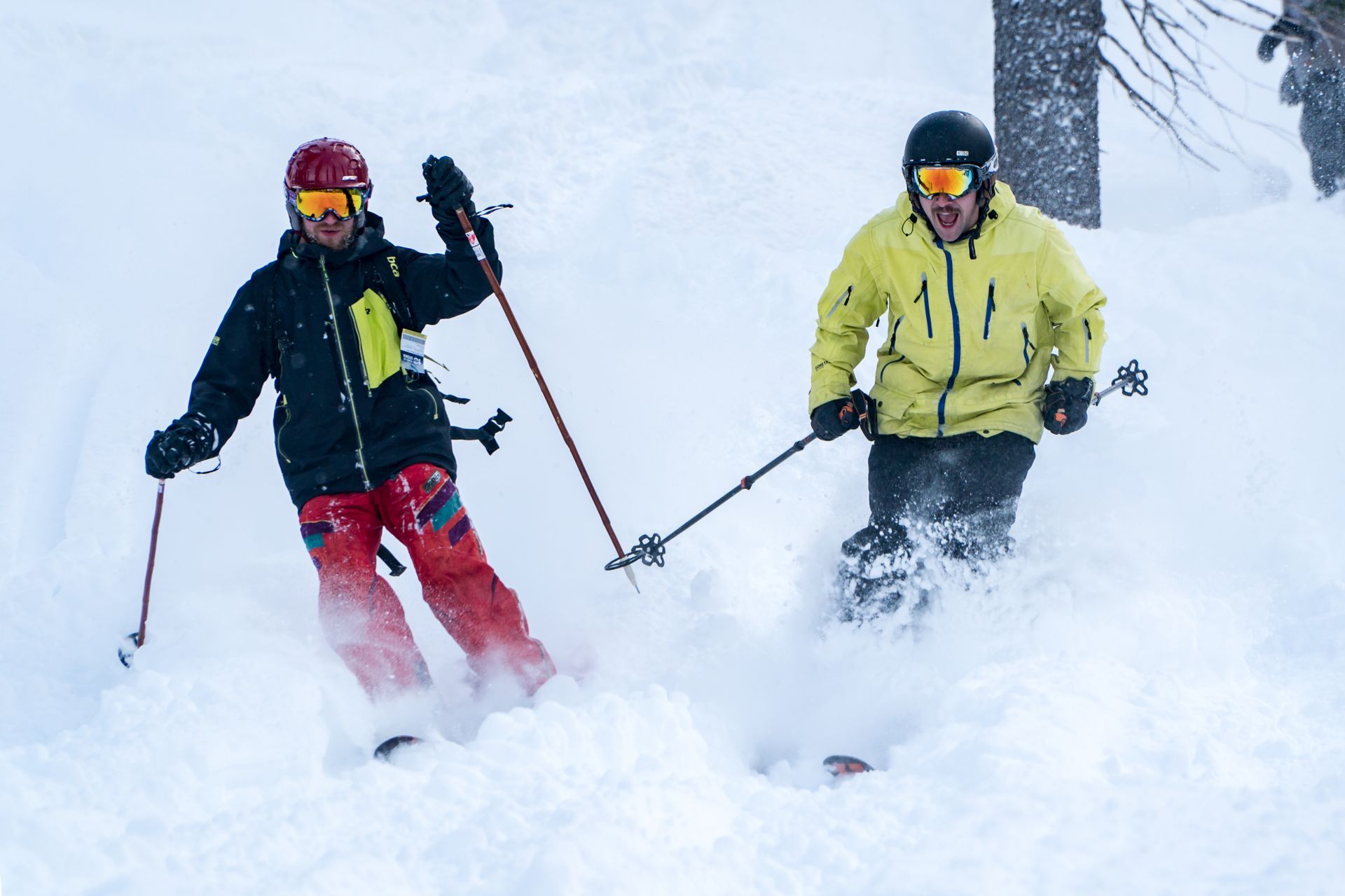 Two skiers in a snowy blizzard, one in red and black, one in yellow, skiing through deep powder