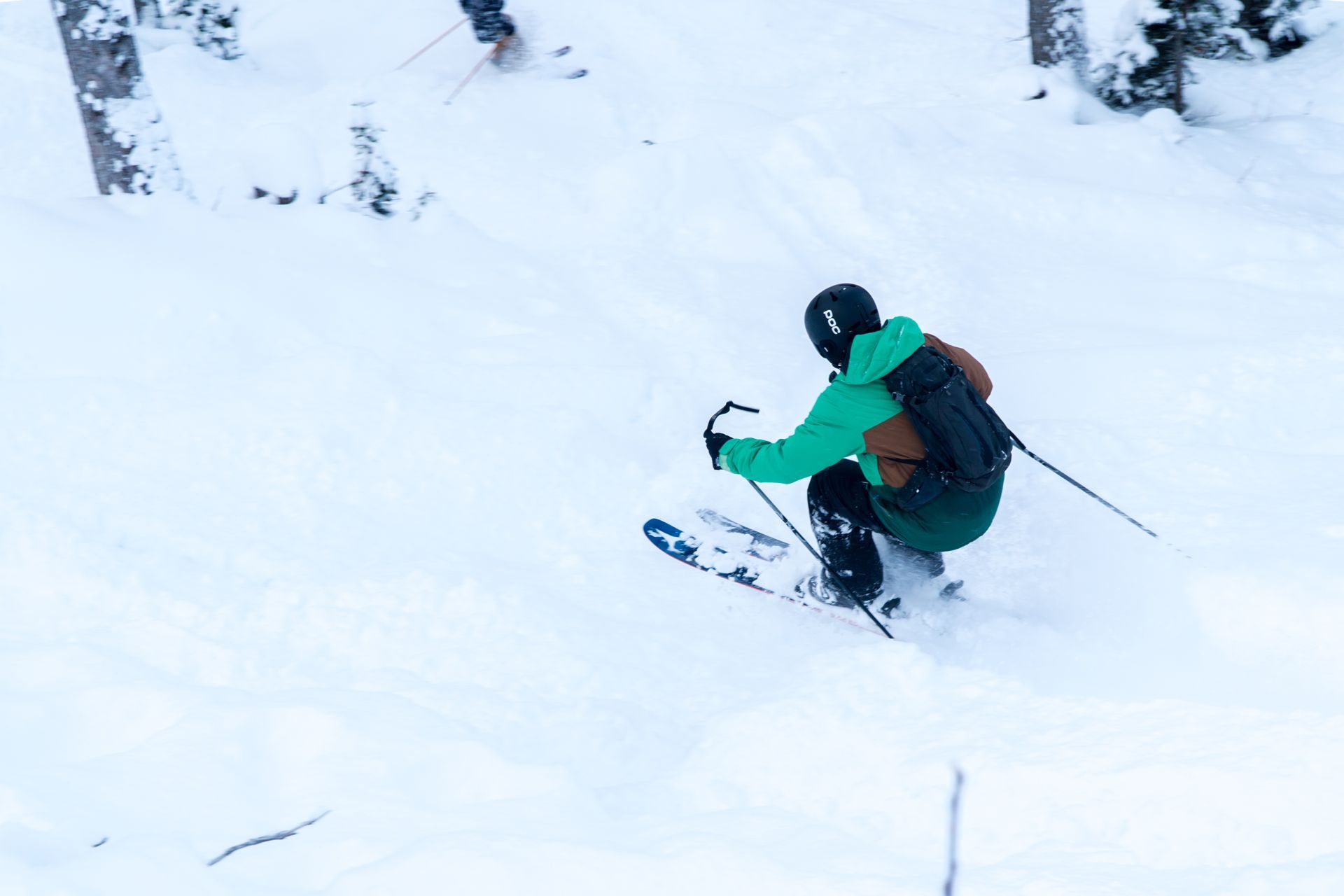 Skier in a green jacket carving down a snowy slope with ski poles.